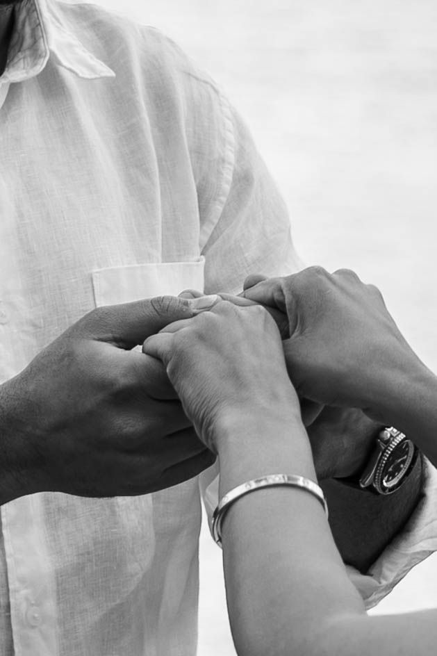 Black and white photo of two people holding hands, one wearing a bracelet and watch, in a tender moment.