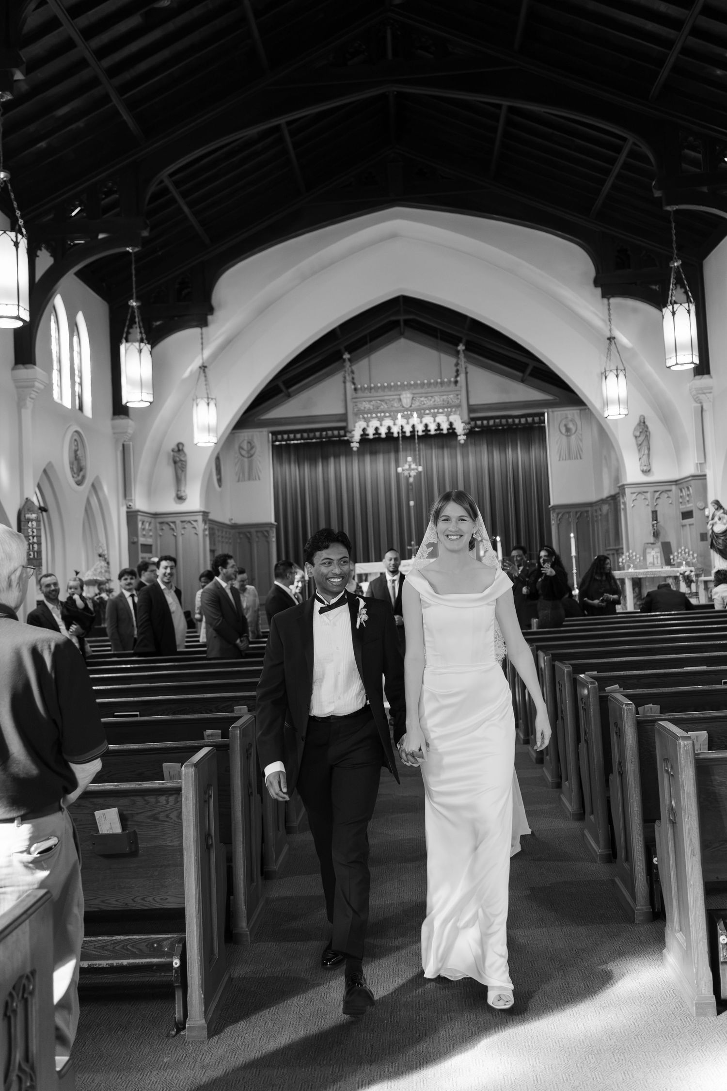 Black and white photo of a newlywed couple walking down the church aisle after their wedding ceremony.