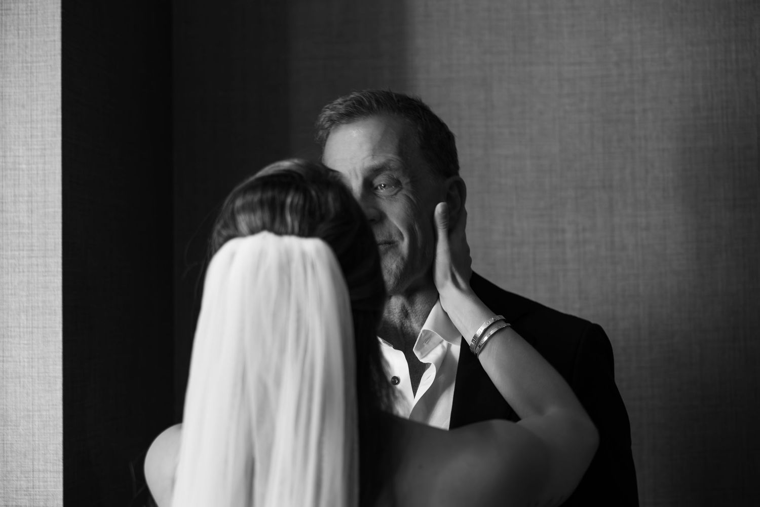 Black and white photo of a bride tenderly touching the face of an emotional older man, likely her father, on her wedding day.