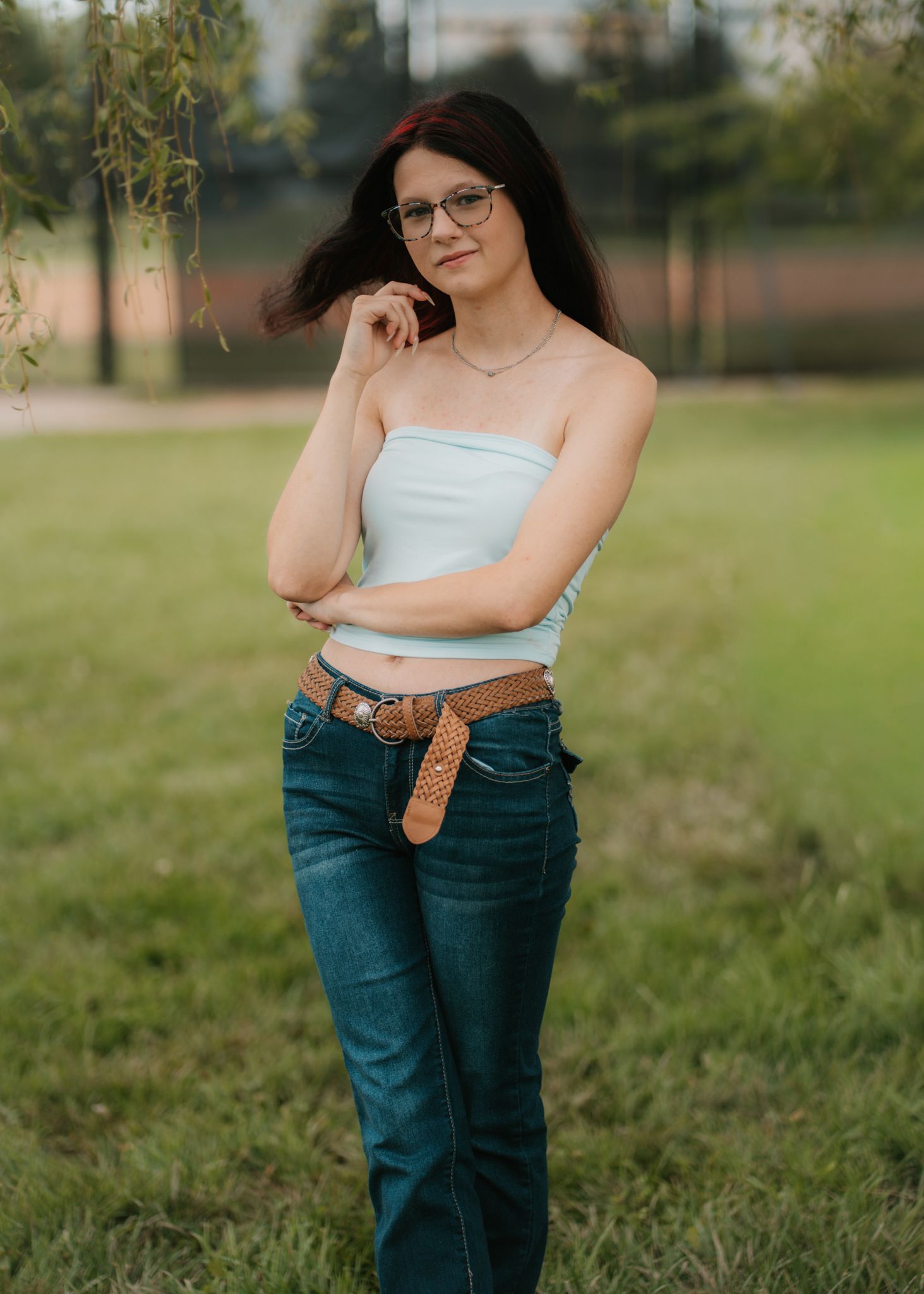 Young woman in white crop top and jeans with brown belt posing outdoors.