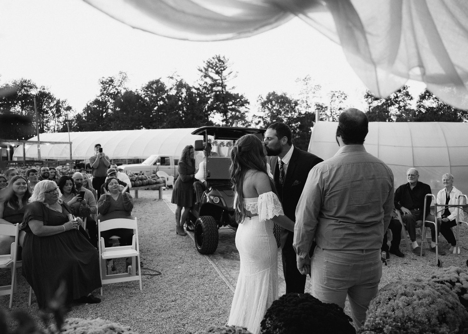 Black and white wide shot of outdoor wedding ceremony with seated guests under draped canopy.
