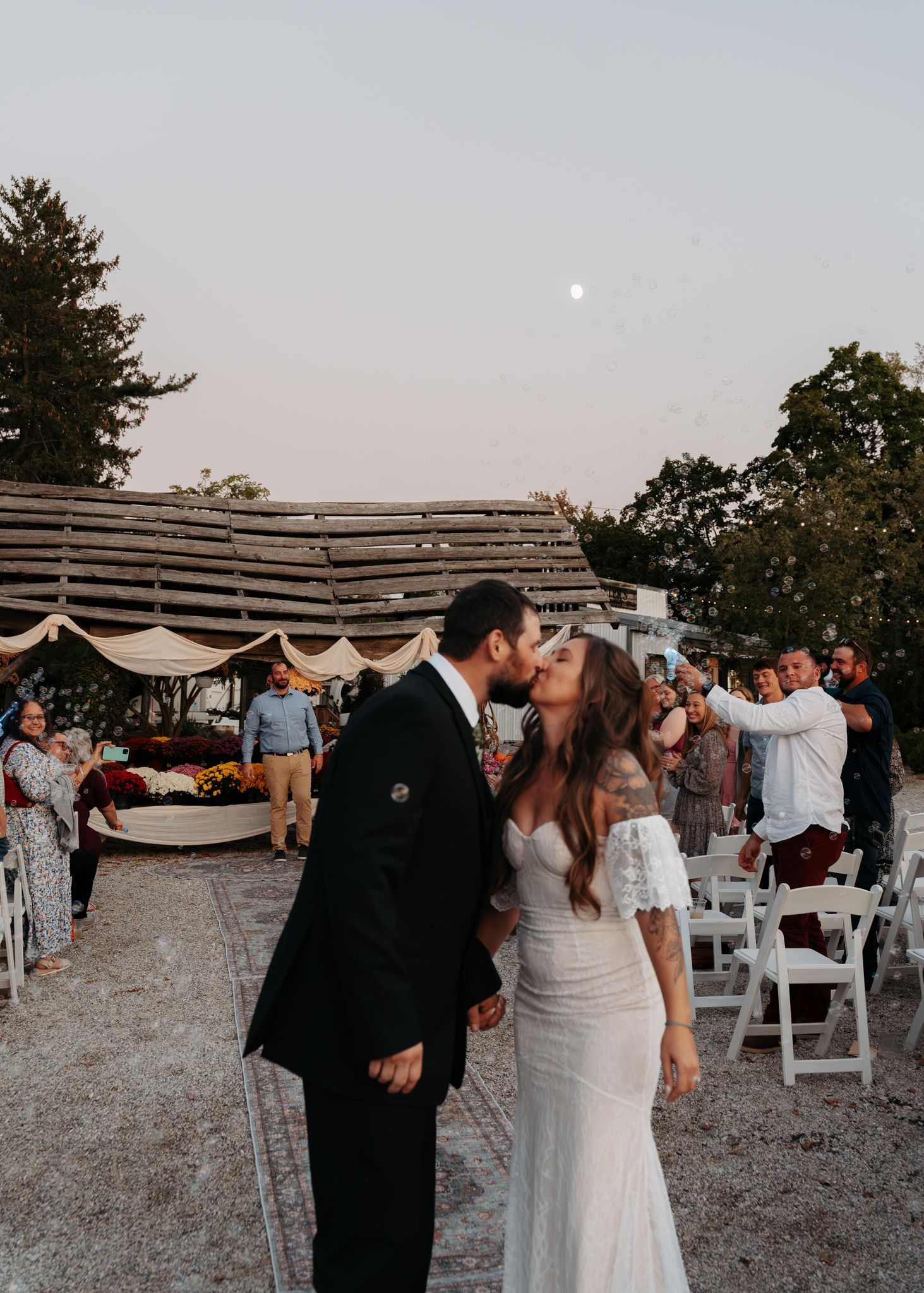 Newlyweds sharing first kiss as married couple during outdoor fall wedding ceremony at dusk.
