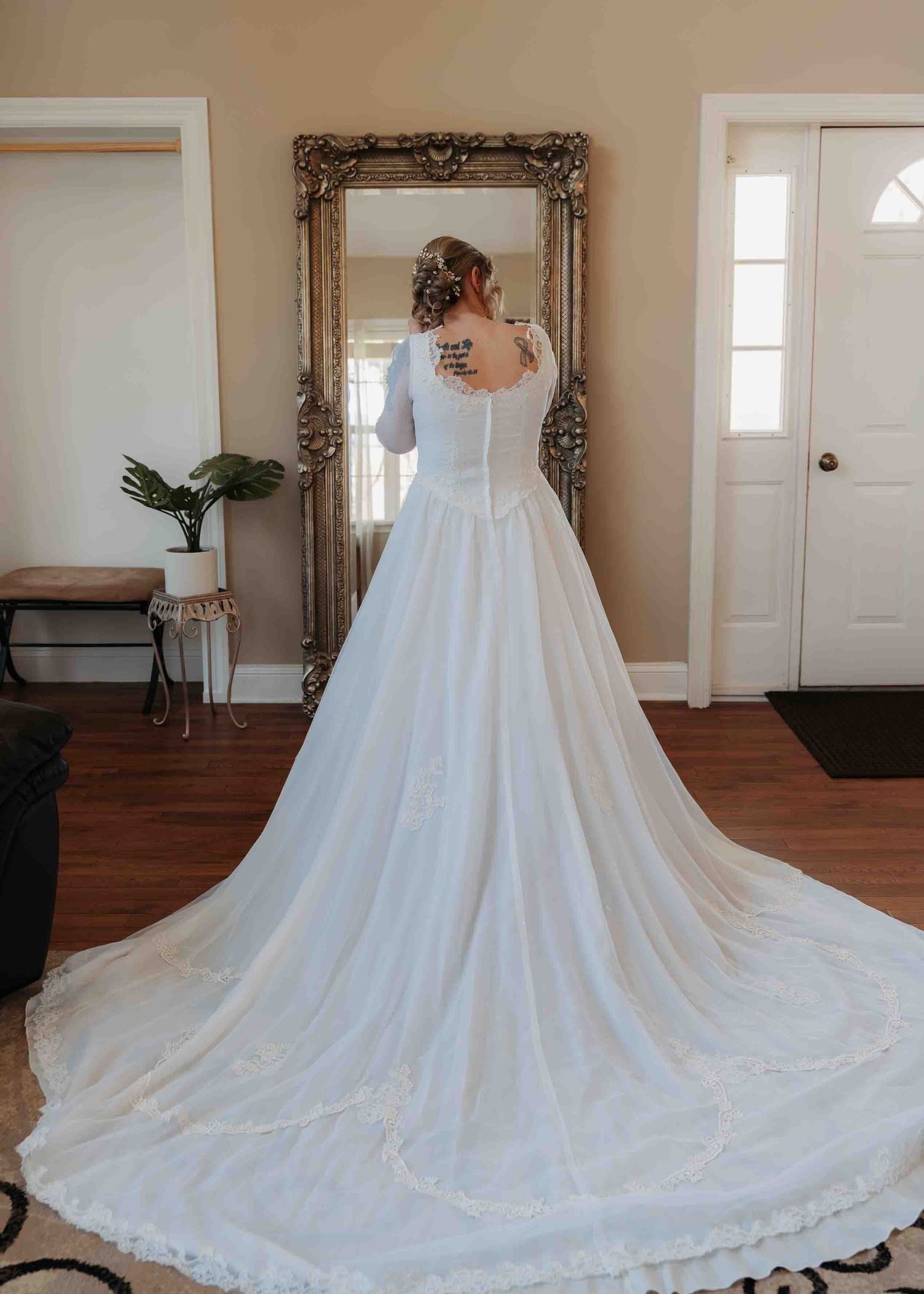 Bride in elegant long-train white wedding gown viewed from behind in mirror.