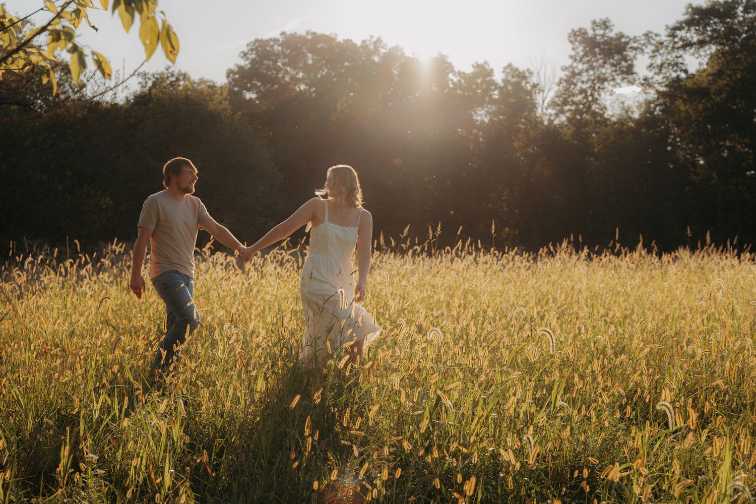 Couple holding hands running through golden sunlit field at sunset in romantic outdoor setting.