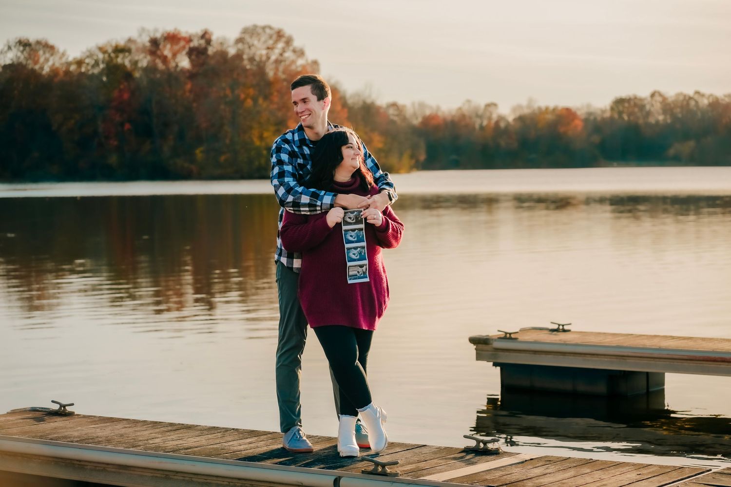 Couple embracing on a wooden dock by a lake during golden autumn sunset.