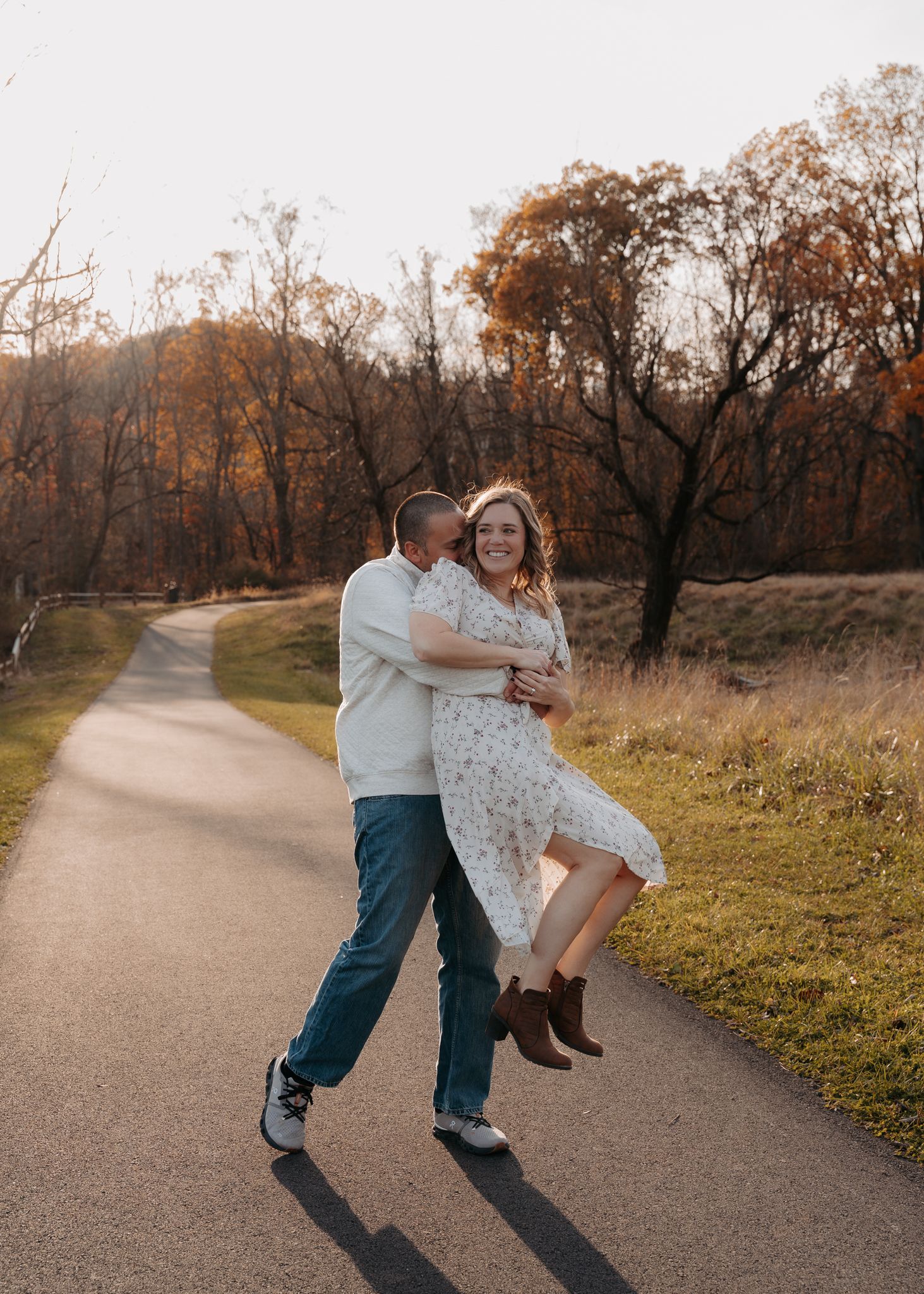Couple dancing and laughing on a tree-lined path during a golden autumn sunset.