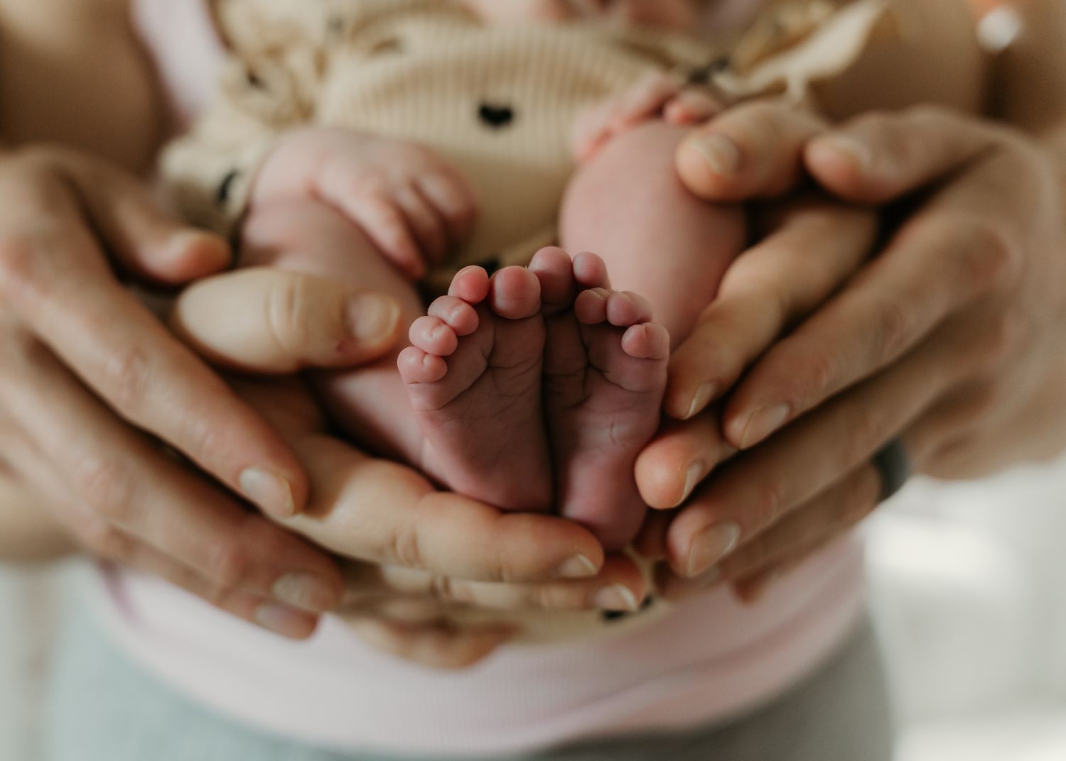 Adult hands gently cradling tiny newborn baby feet in a tender close-up portrait.