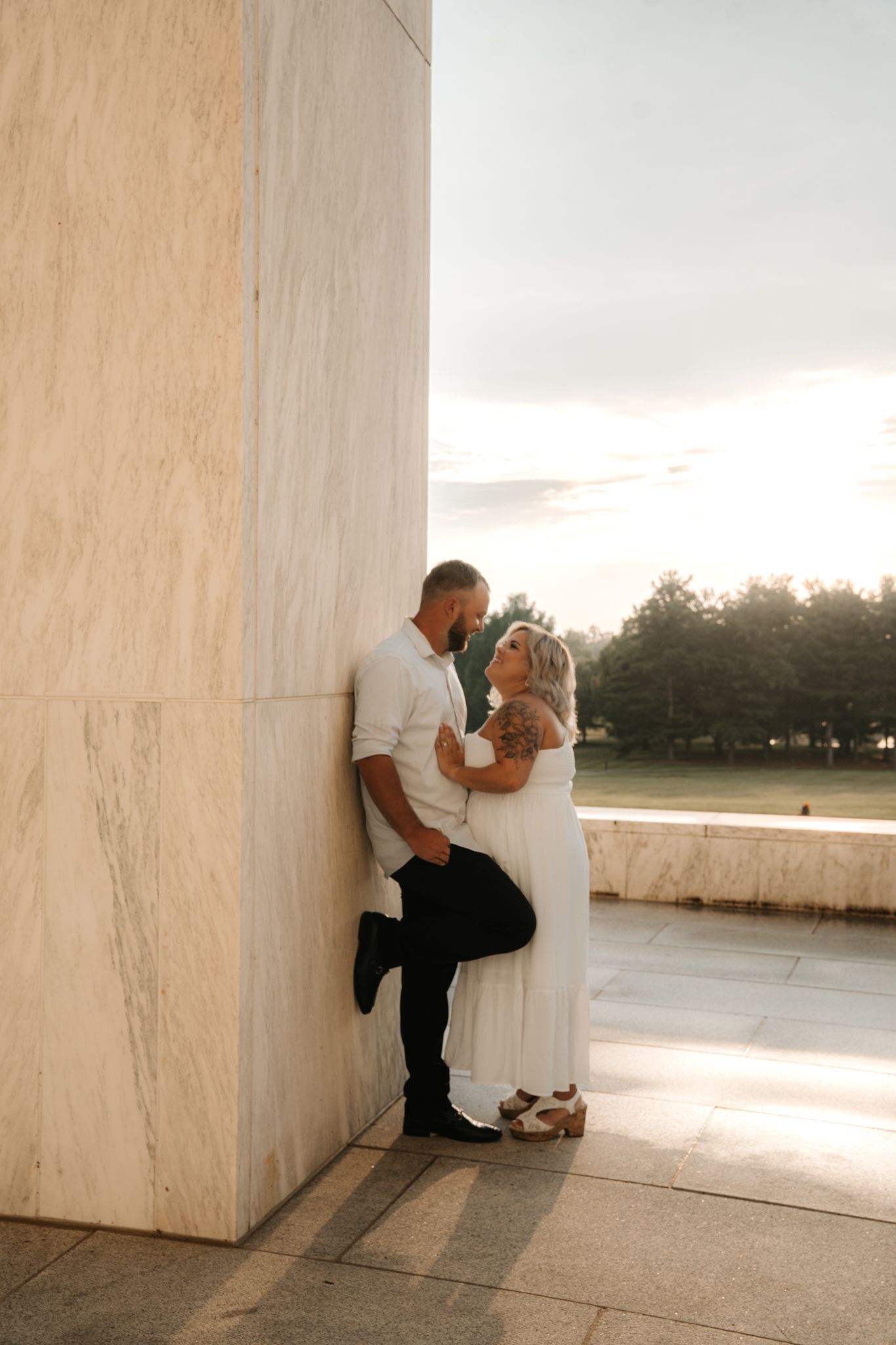 Couple sharing a romantic moment leaning against a marble column at golden hour.