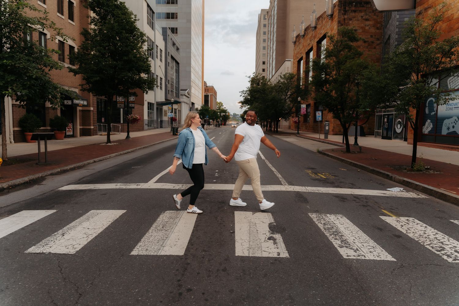 Couple holding hands while crossing a zebra crosswalk on an empty urban city street.