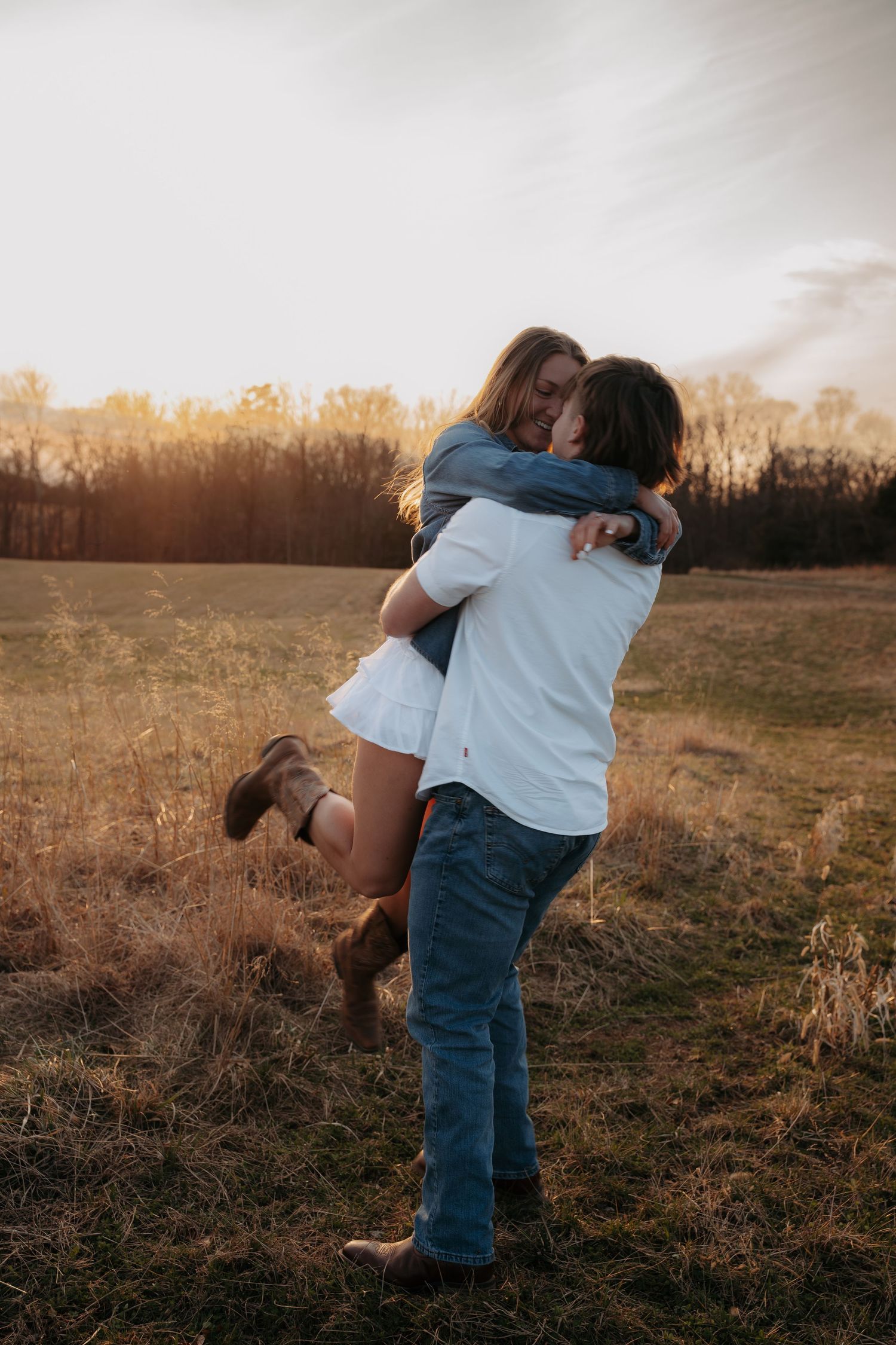 Man lifting woman in a romantic embrace in a golden sunset field.