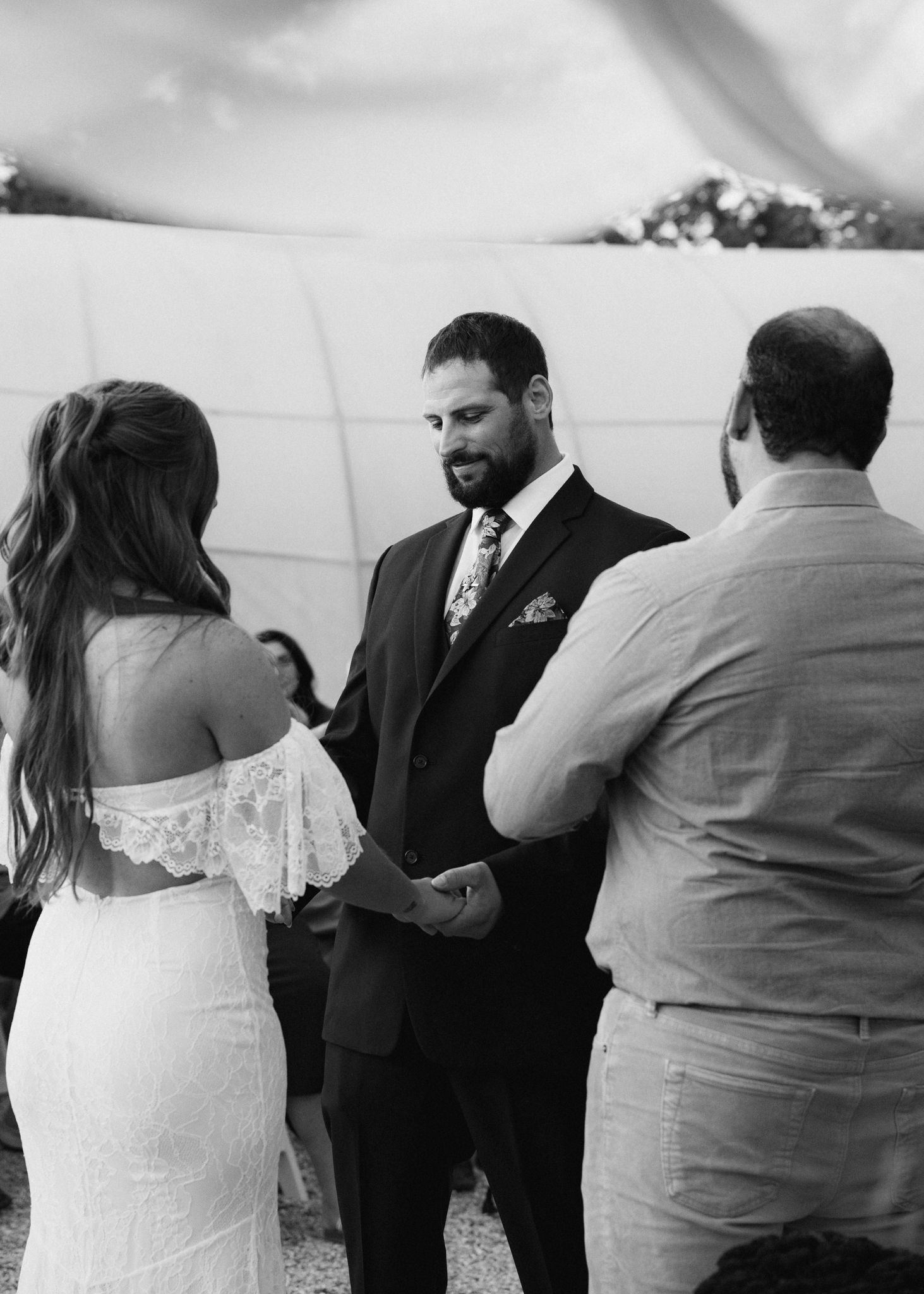 Black and white photo of groom holding bride's hands during outdoor wedding ceremony.