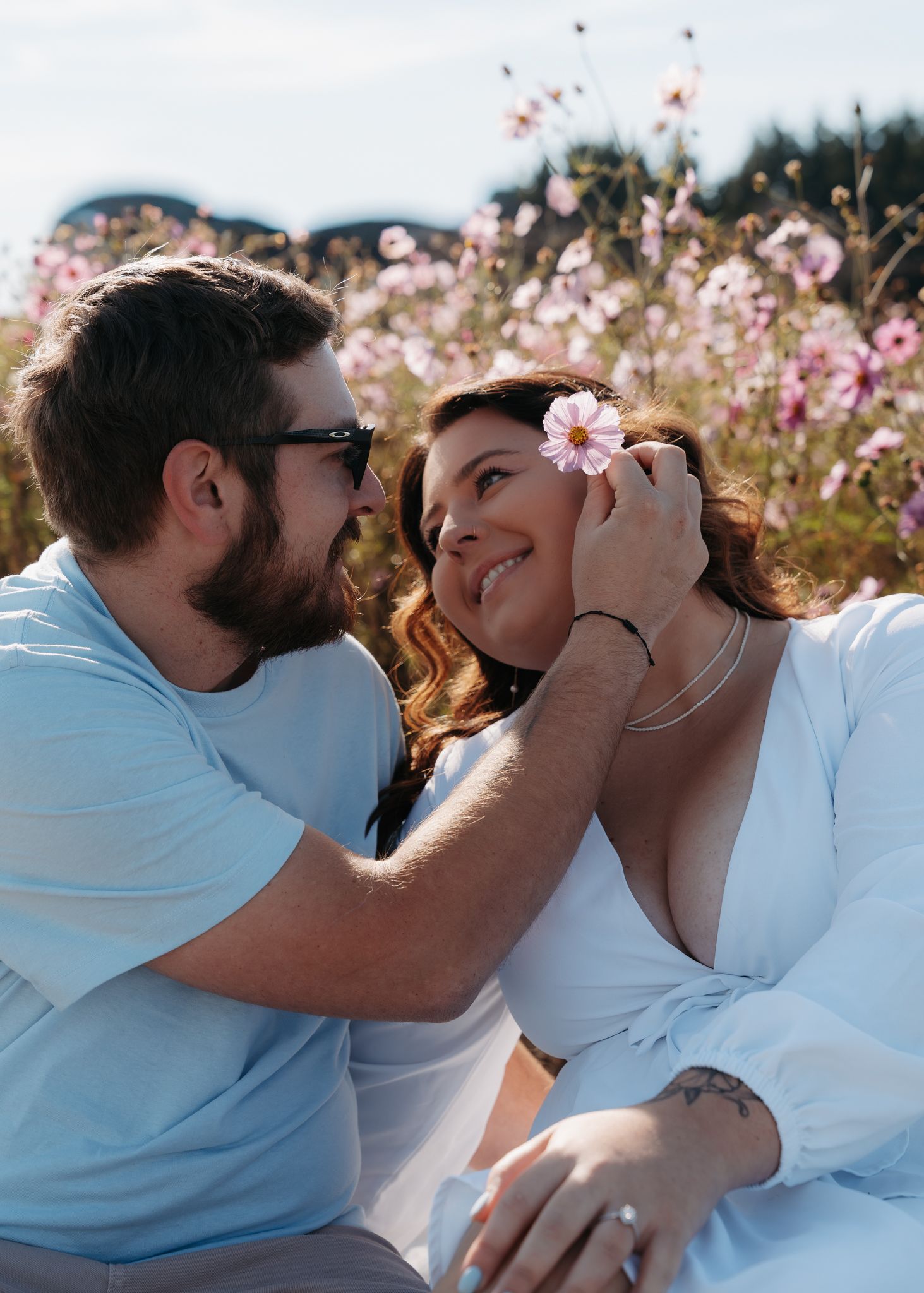 Couple sitting in a flower field, man placing a pink bloom in womans hair.