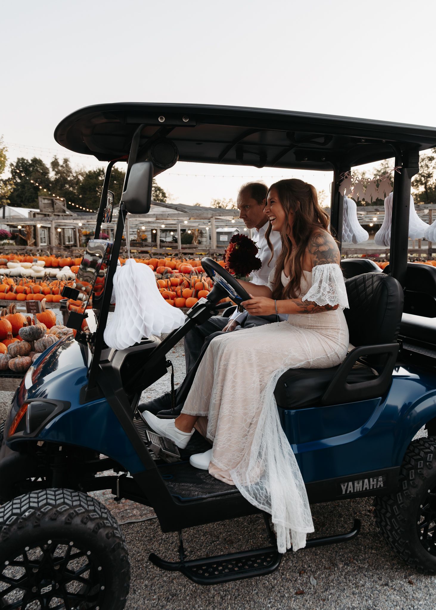 Bride and groom riding blue Yamaha golf cart through pumpkin patch at sunset.