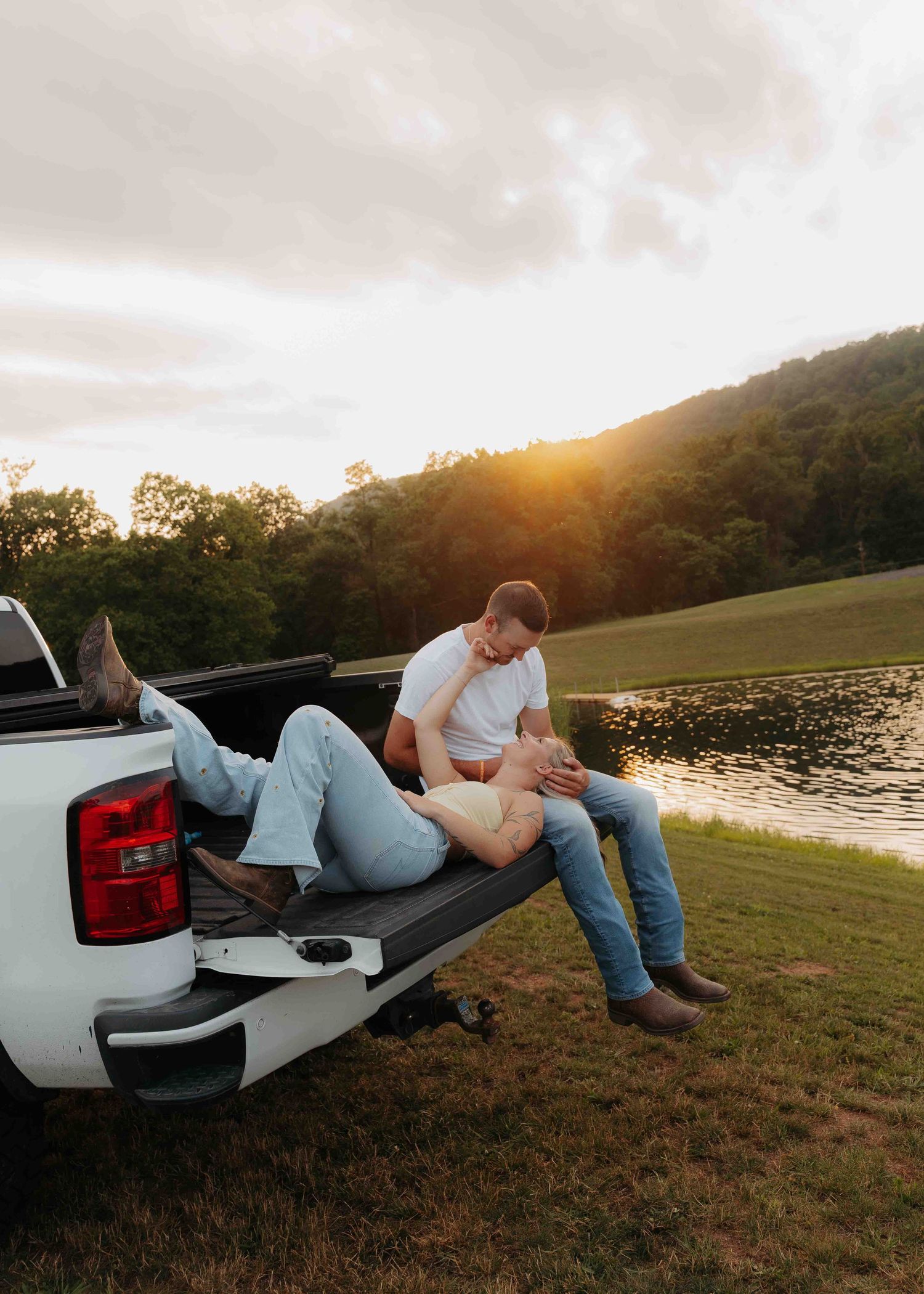 Romantic couple relaxing on a truck tailgate by a lake at golden sunset.