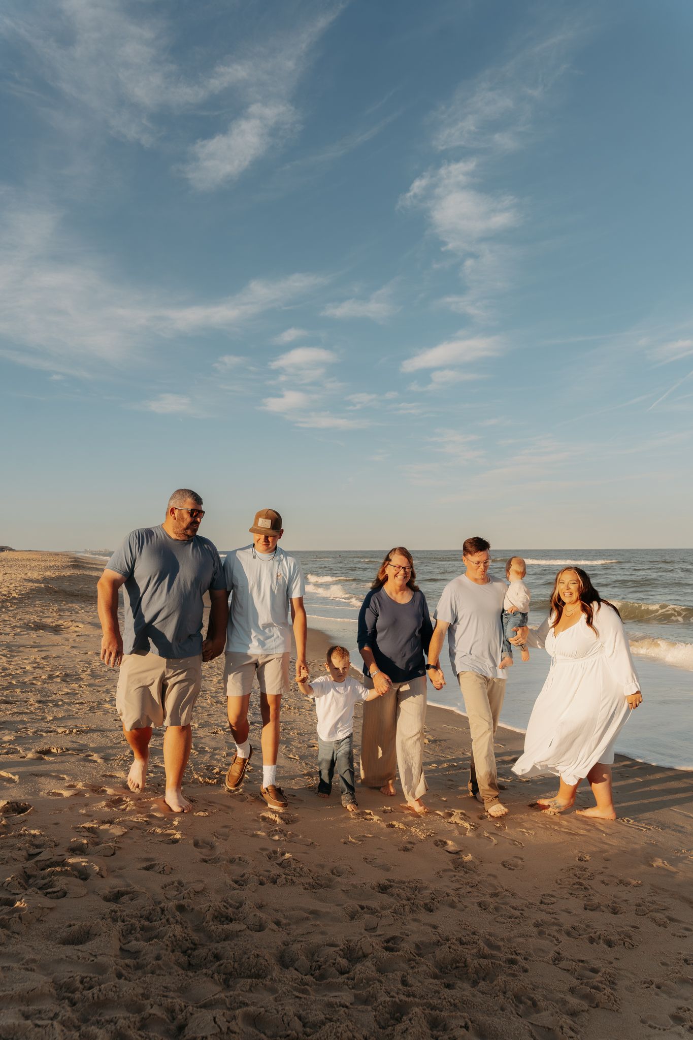 Large family walking together barefoot on sandy beach during golden hour sunset photography session.