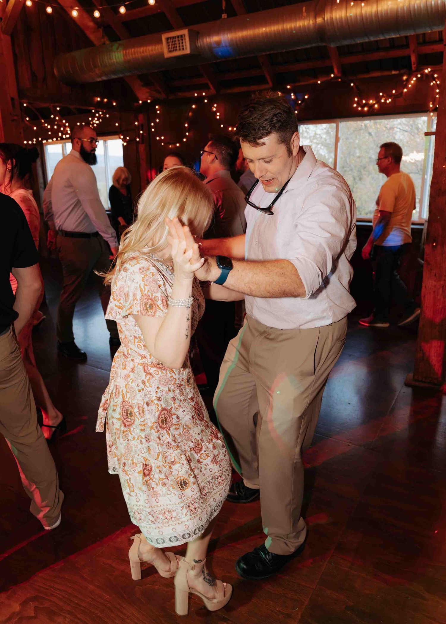 Couple slow dancing together at a wedding reception in a rustic barn with string lights.