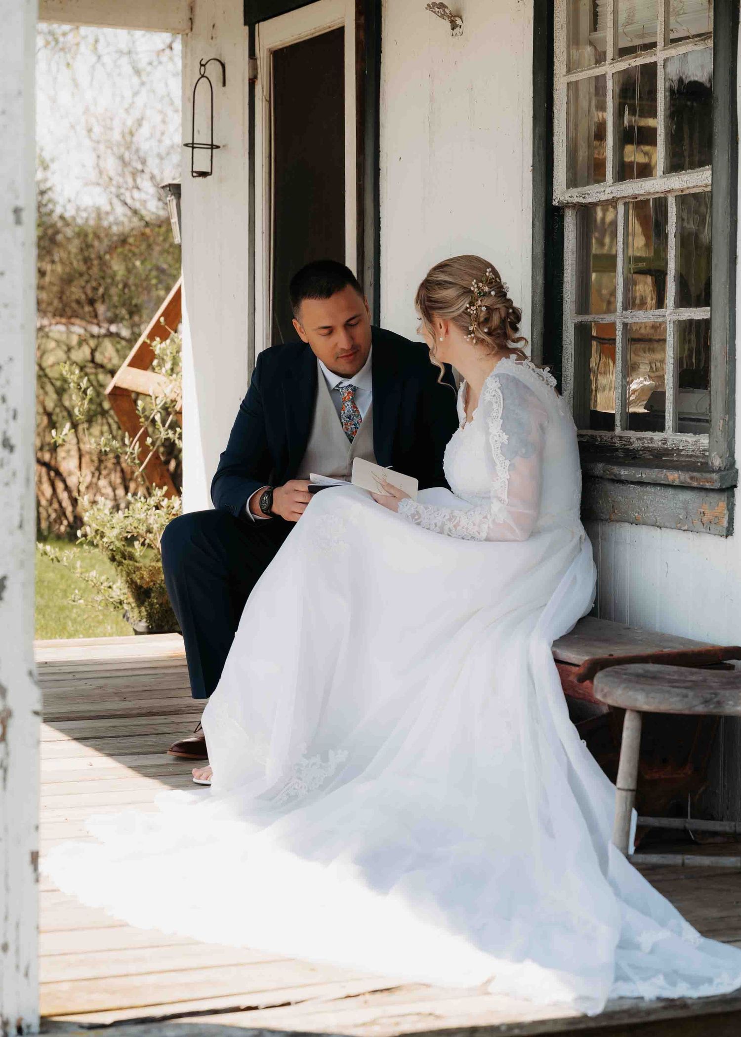 Bride and groom sit on rustic porch reading vows together before wedding ceremony.
