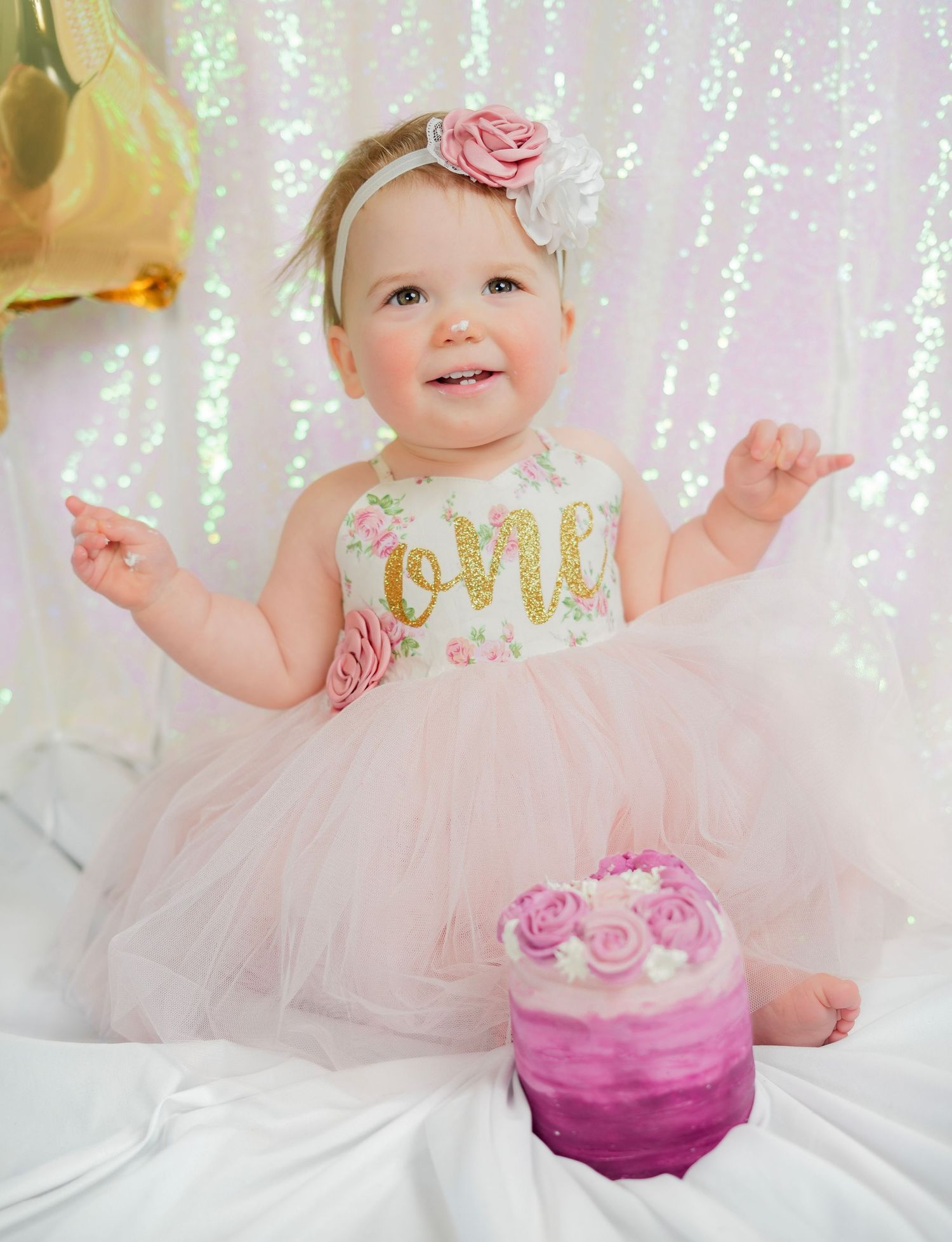 Baby girl in pink tutu dress celebrating her first birthday with a small cake.