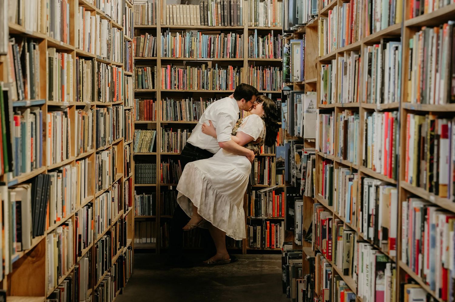 Couple sharing a romantic dip kiss in the aisle of a cozy bookstore.