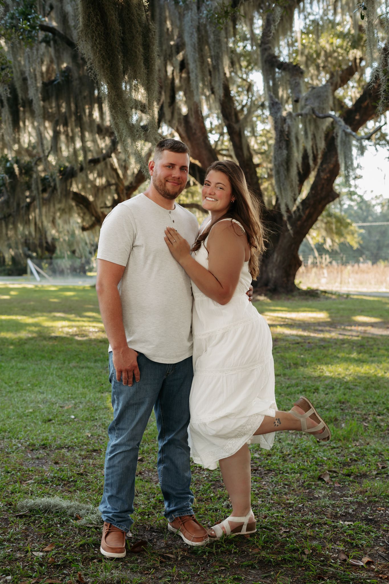 Smiling couple posing together under a large moss-draped oak tree outdoors.