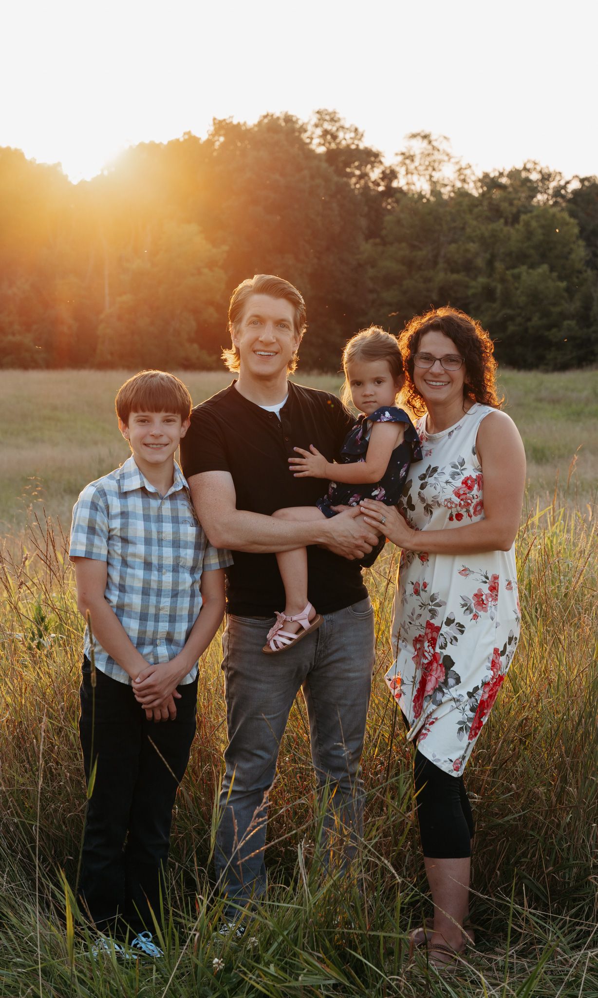Family of four posing together in a sunlit field with warm golden backlight.
