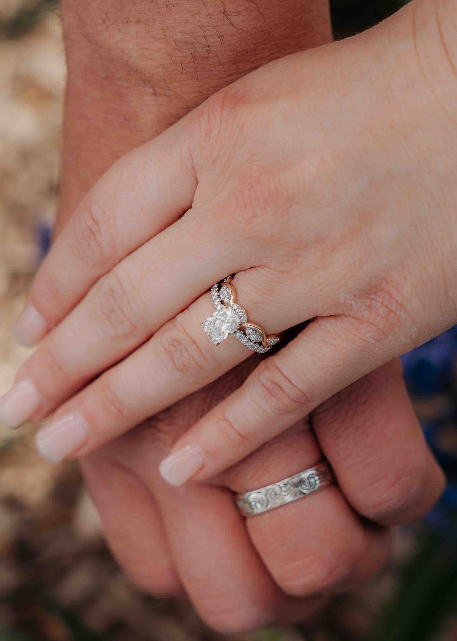 Close-up of bride's diamond twist engagement ring and groom's engraved wedding band as couple holds hands.