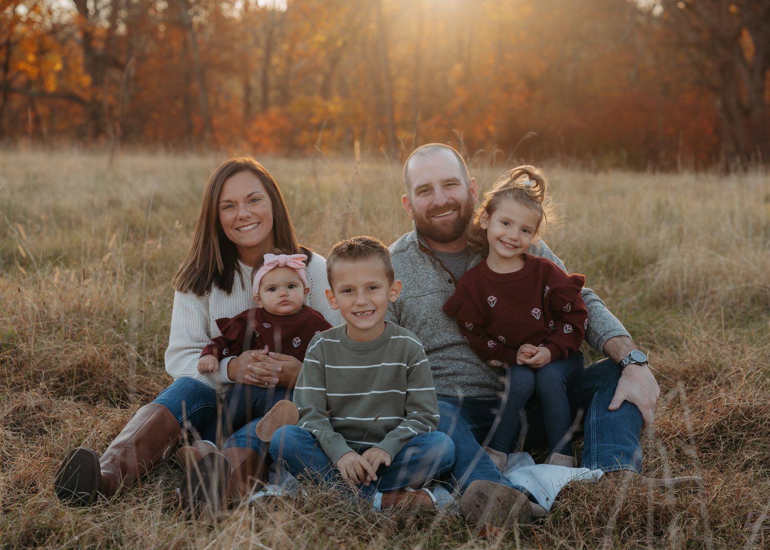 Happy family of five sitting together in a golden autumn field at sunset.