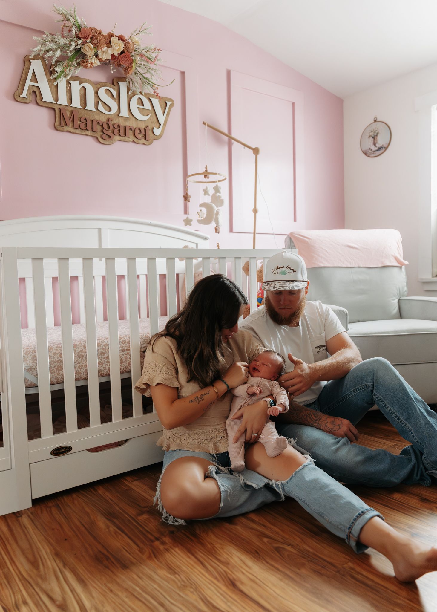 Parents sitting on nursery floor with newborn beneath Ainsley Margaret name sign.
