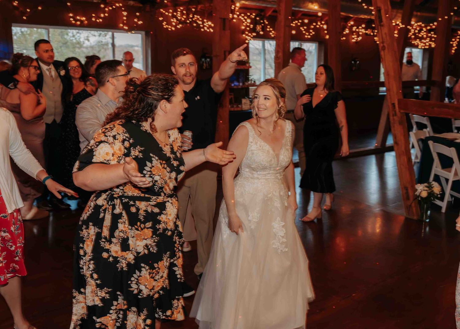 Bride in lace gown dancing joyfully with guests at rustic barn wedding reception.