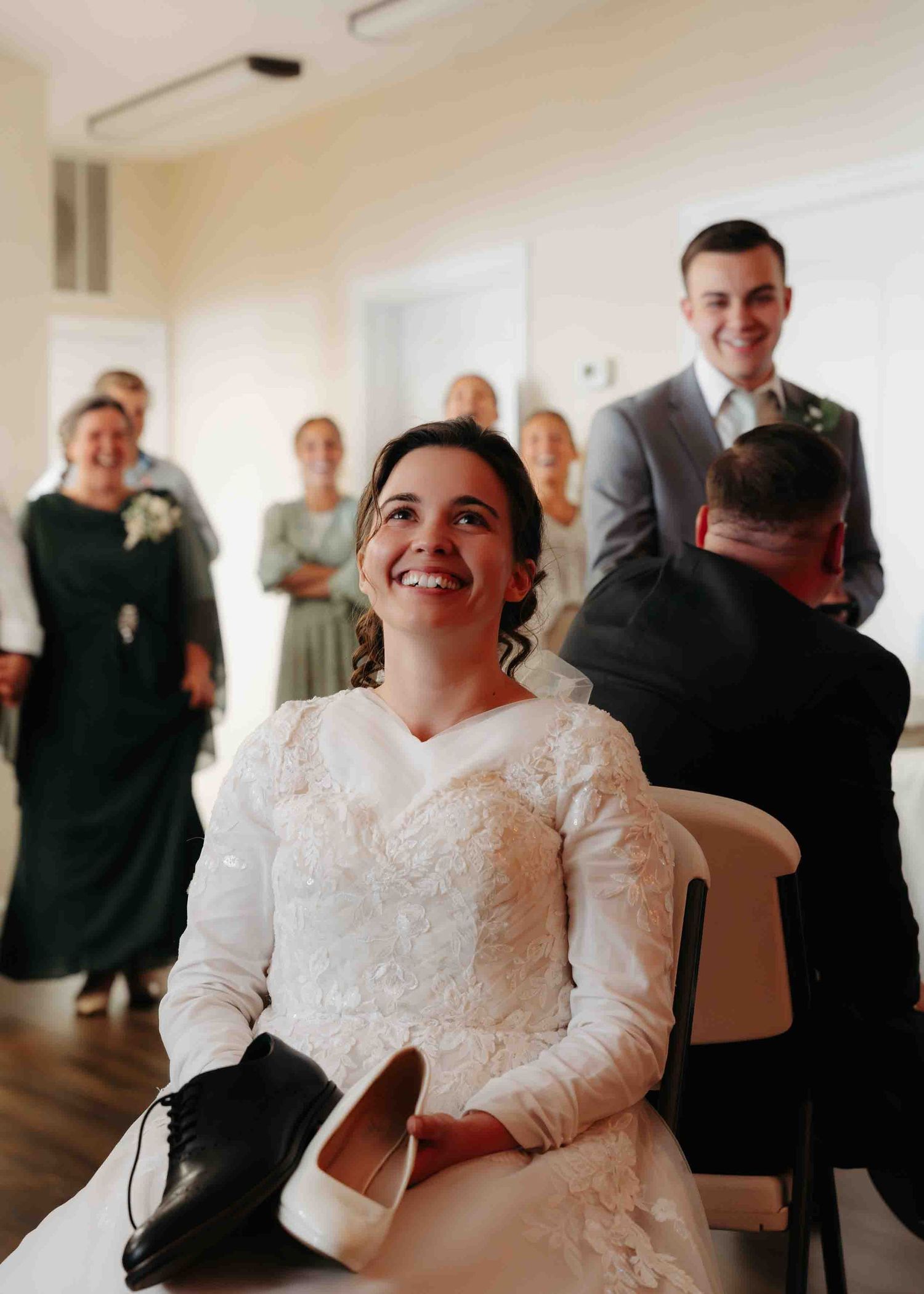 Radiant bride in lace gown laughs joyfully while seated during wedding reception.