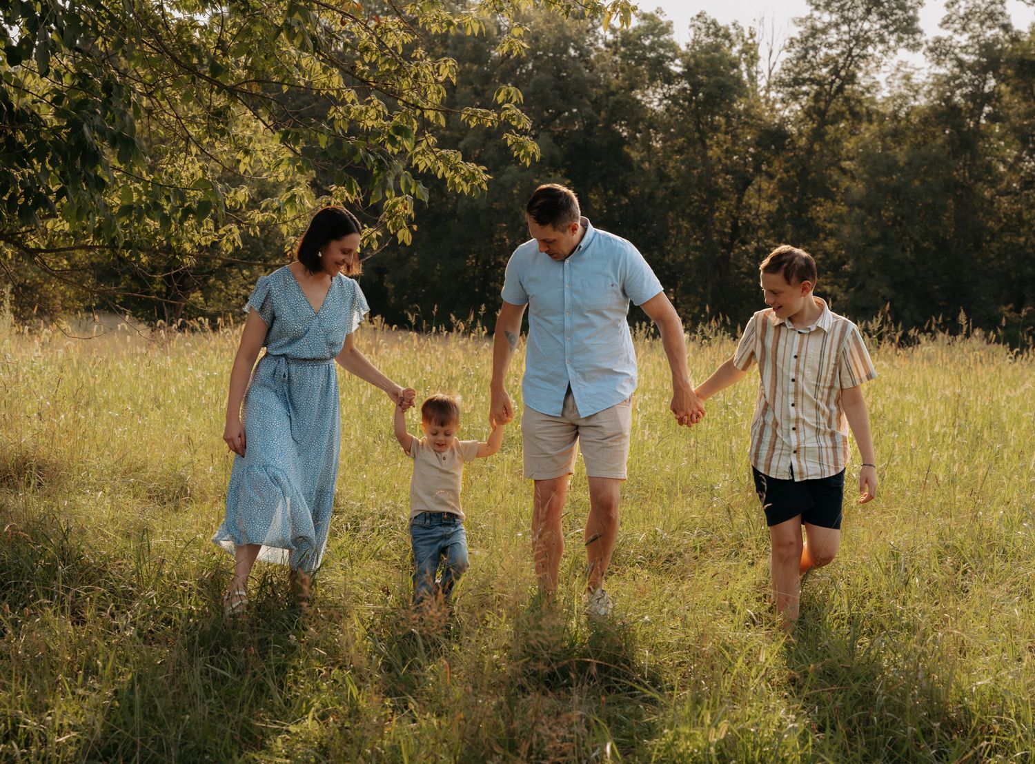 Happy family of four walking hand in hand through a sunny green meadow.