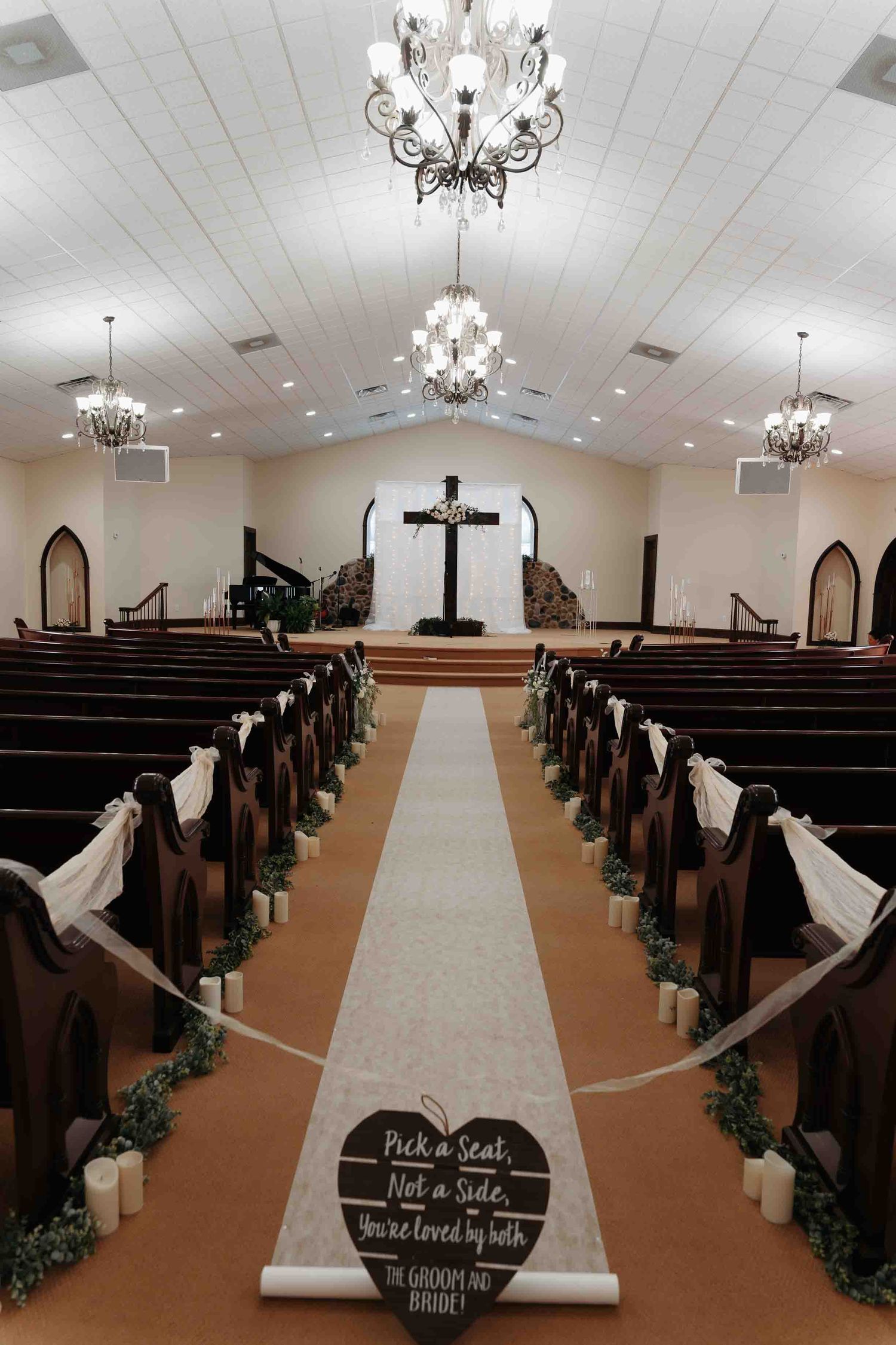 Elegant church wedding aisle with white runner, candles, and wooden pews leading to a cross altar.
