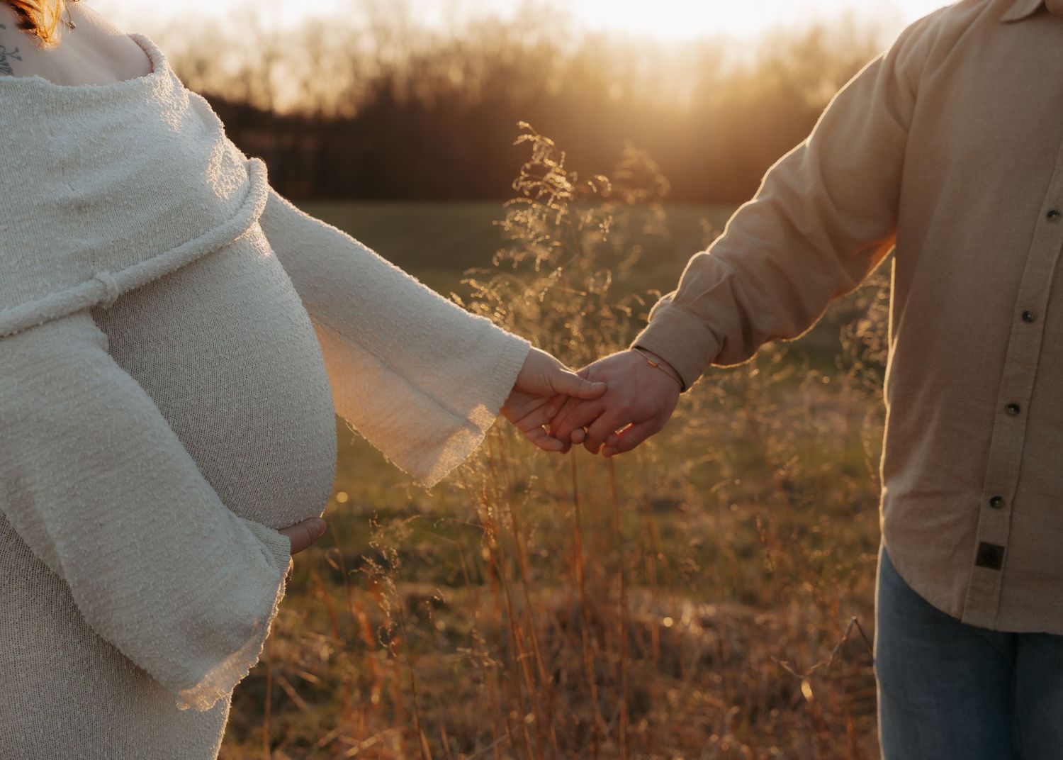 Couple holding hands at sunset in an open field, wearing cozy winter sweaters.