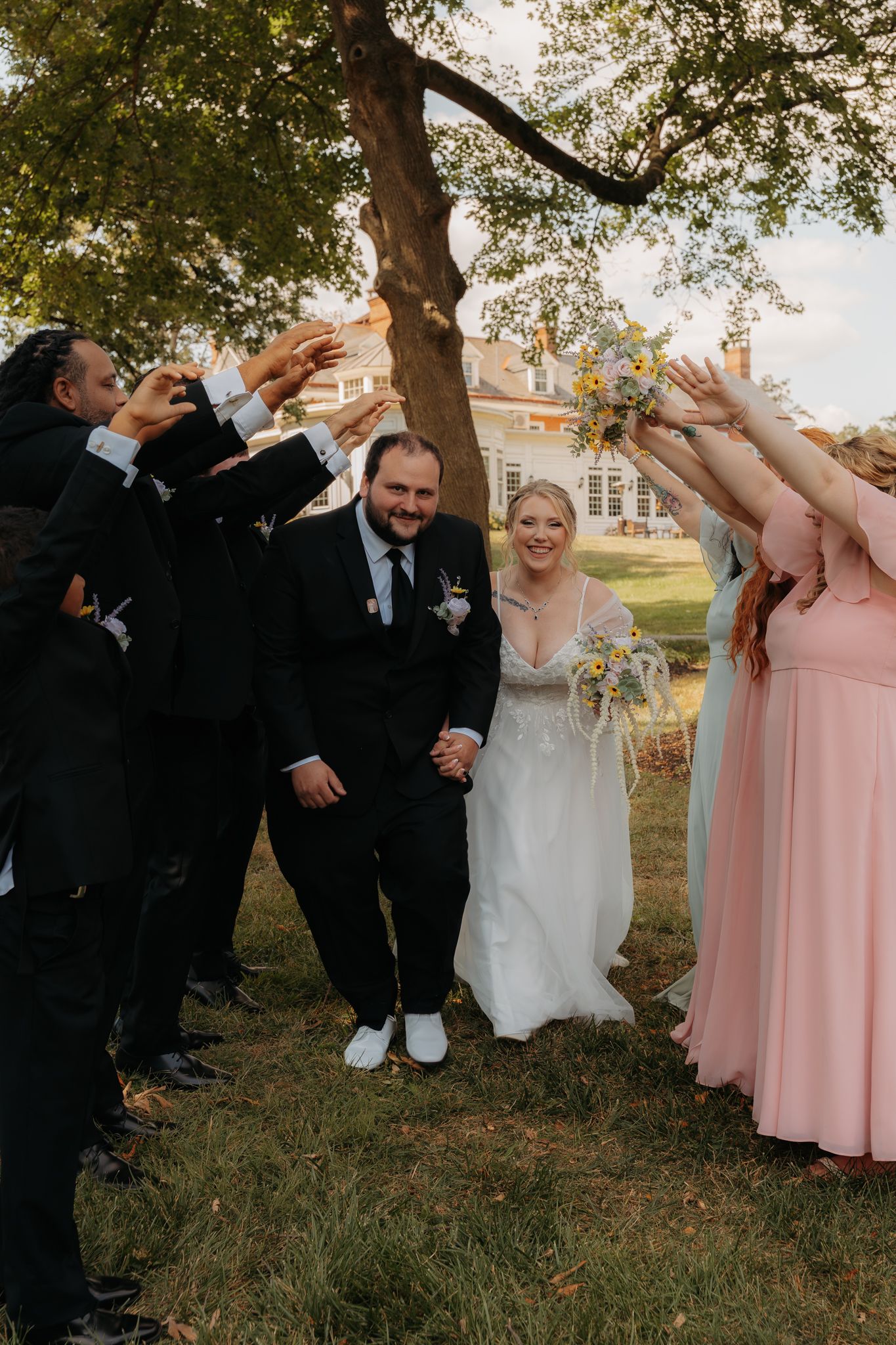 Wedding party tunnel with bridesmaids in pink and groomsmen in black suits cheering as bride and groom walk through.