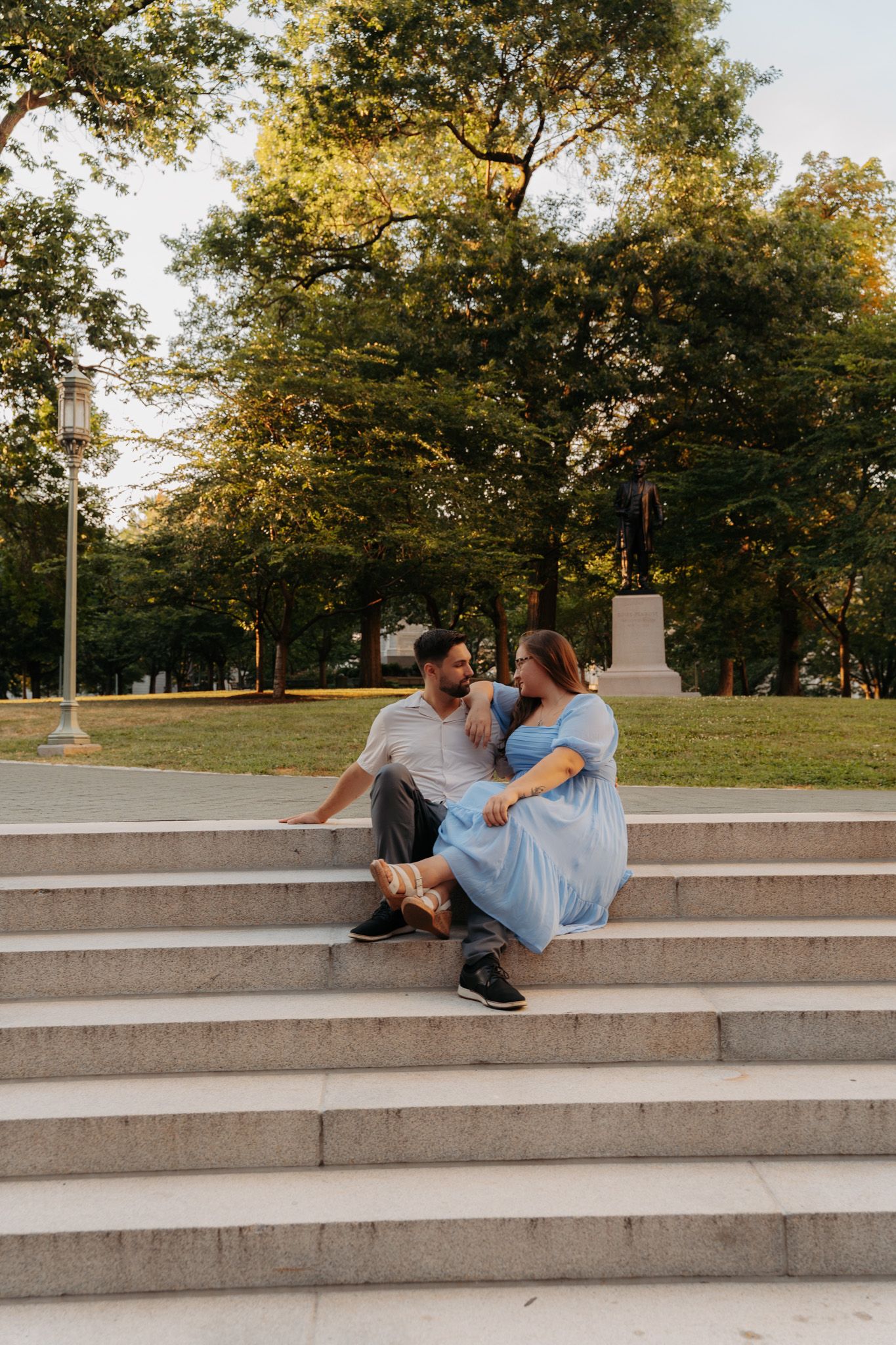 Couple sitting together on park steps, woman in light blue dress and man in white shirt sharing a moment.