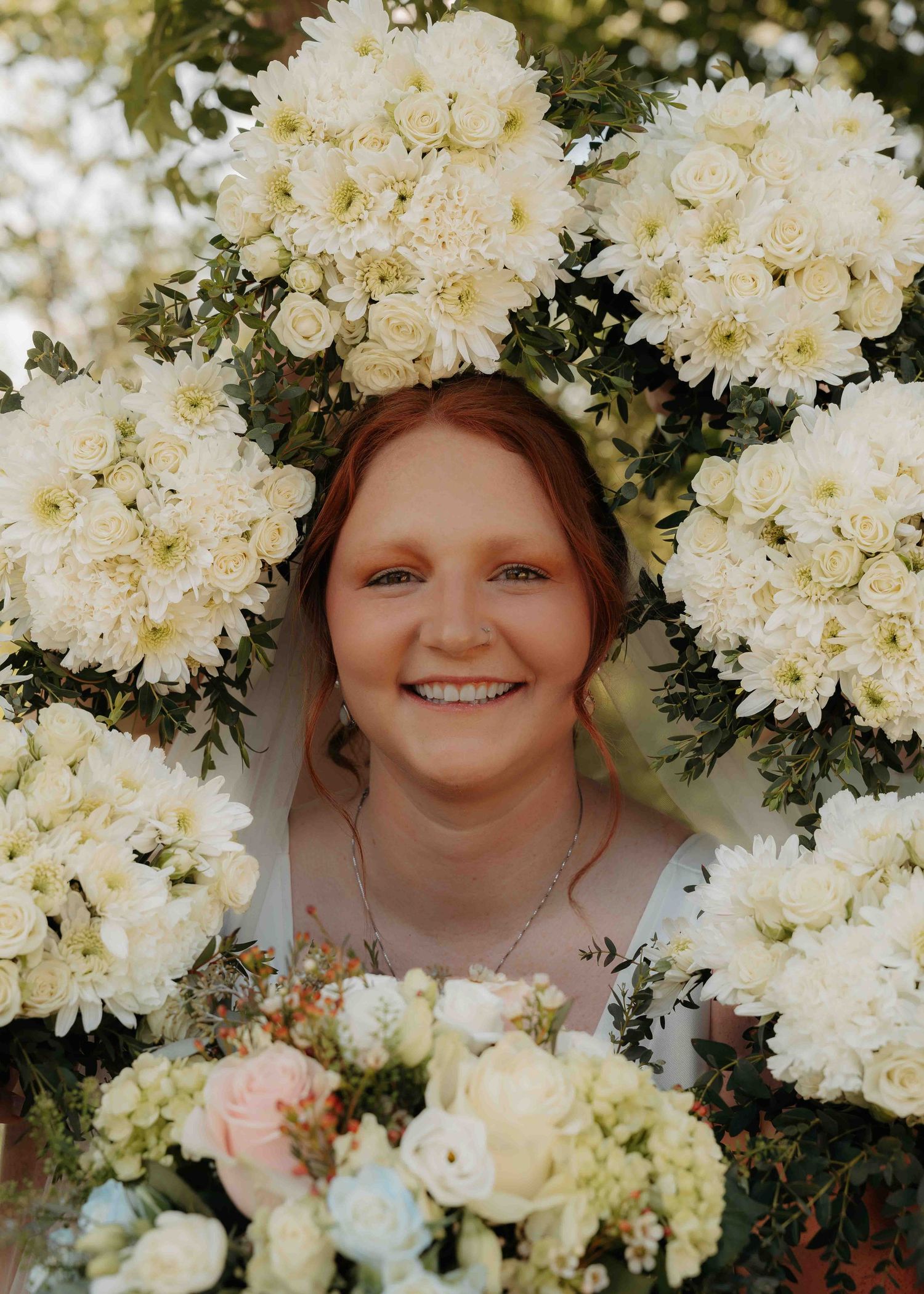 Smiling red-haired bride surrounded by lush white floral bouquets of roses and chrysanthemums.