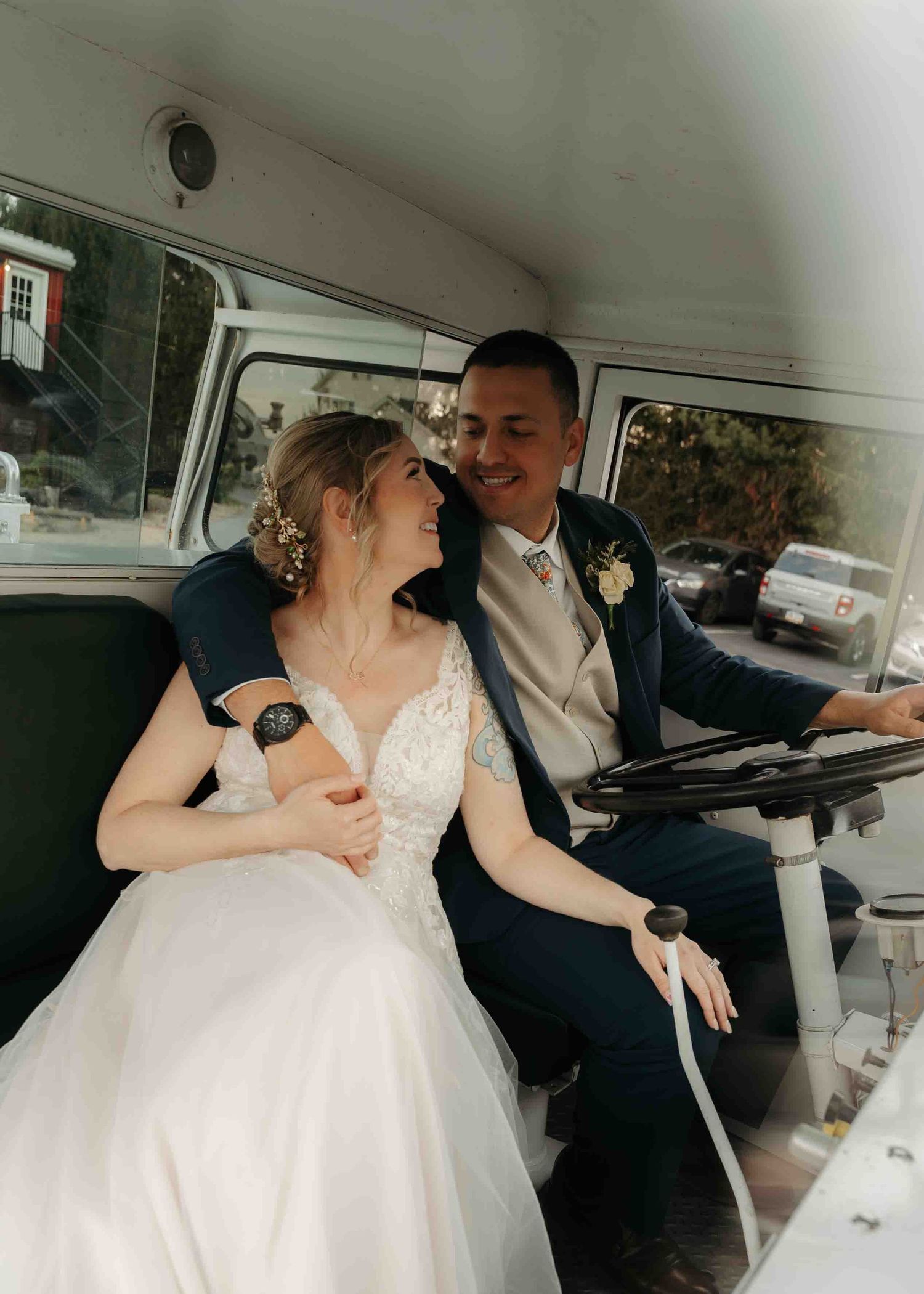 Bride and groom sitting together smiling inside vintage white bus at wedding.