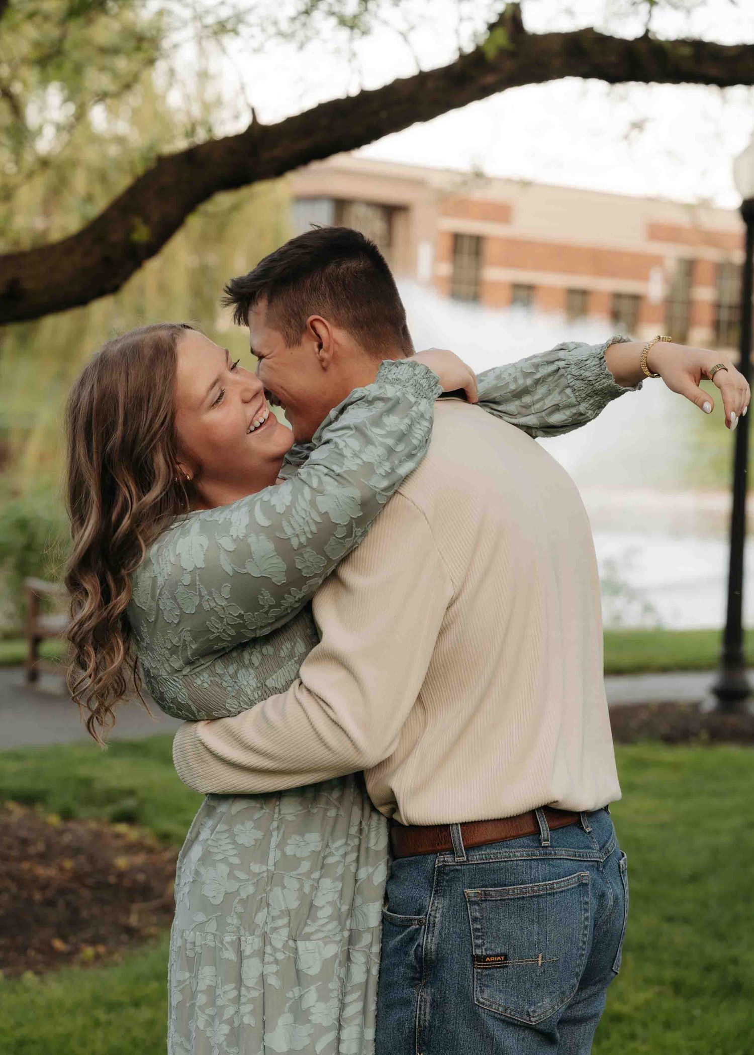 Happy couple embracing and laughing under a large tree in a park setting.