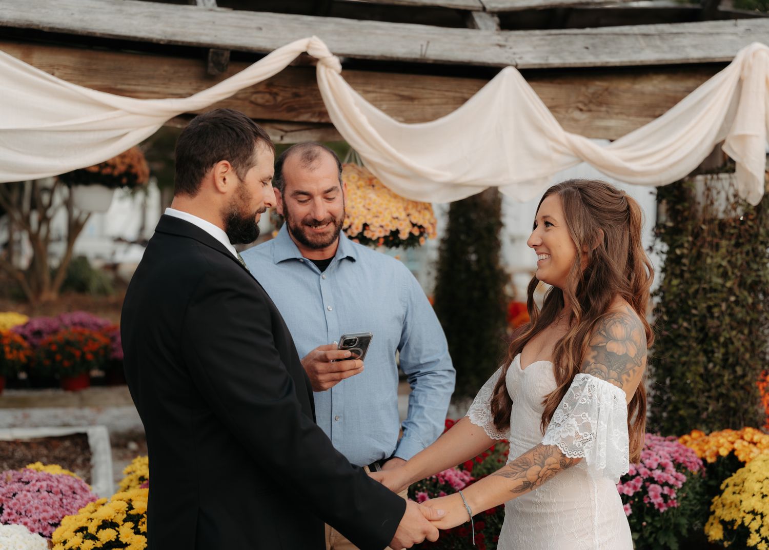 Bride and groom exchanging vows at fall wedding with colorful mums and draping.