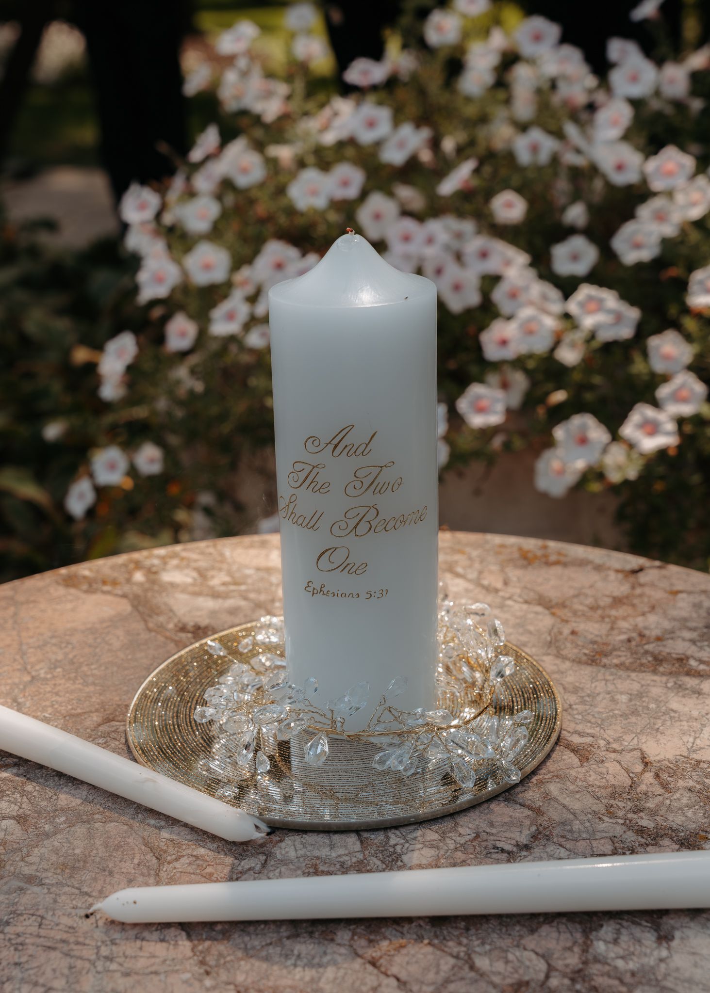 Unity candle engraved with Ephesians 5:31 scripture displayed on a decorative plate with flowers.