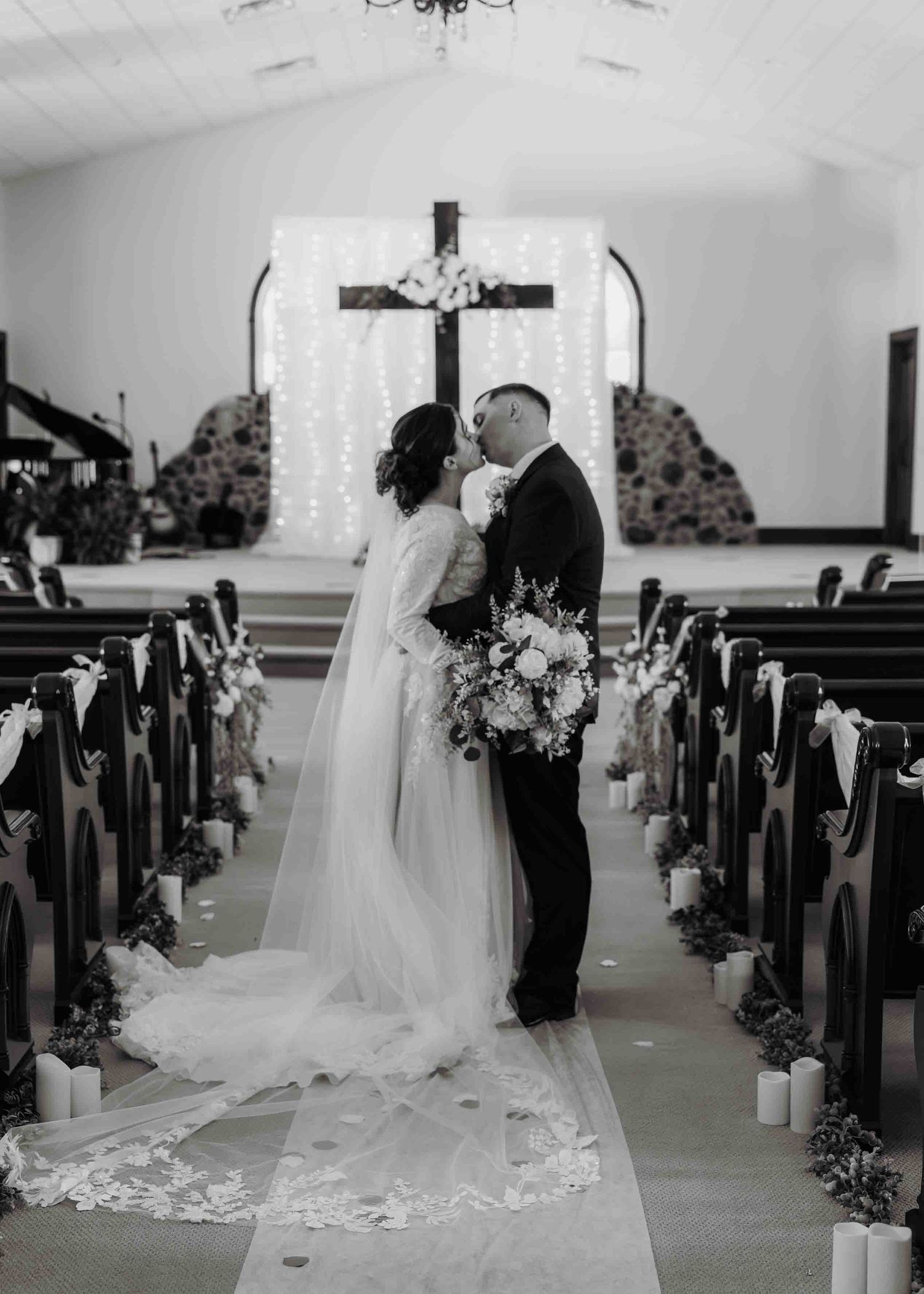 Black and white photo of bride and groom kissing at the altar of a decorated church.