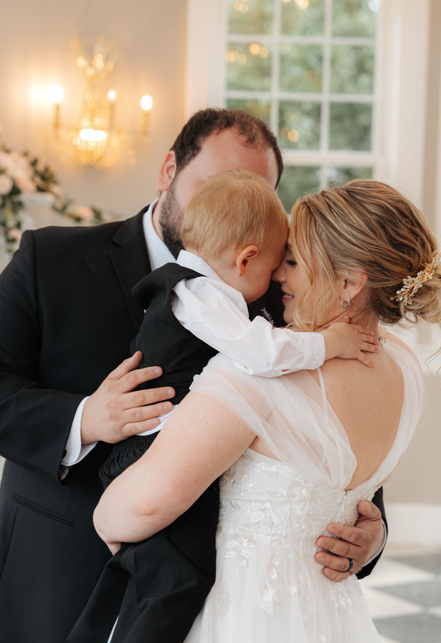 Bride and groom sharing tender moment with baby in tuxedo at elegant wedding ceremony.