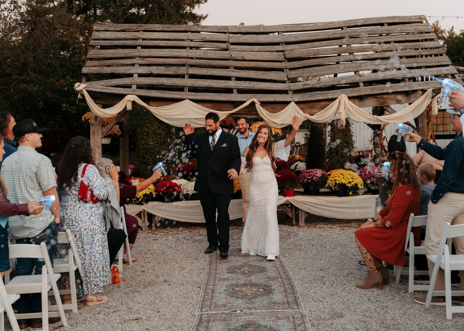 Newlyweds walking down the aisle after outdoor fall wedding ceremony with cheering guests.