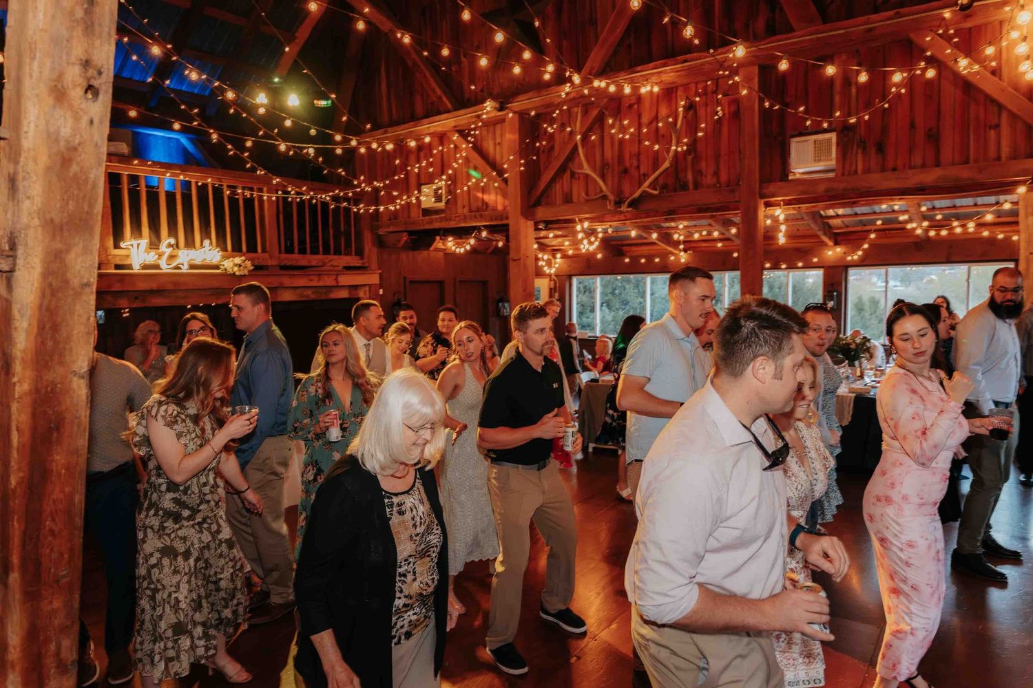 Guests dancing and celebrating at a wedding reception inside a warmly lit rustic barn venue.