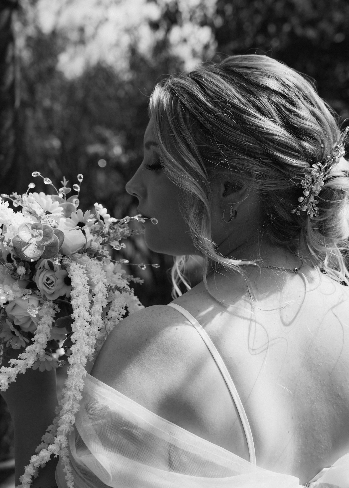 Black and white portrait of bride with floral hair accessories holding bouquet, showing elegant updo hairstyle.