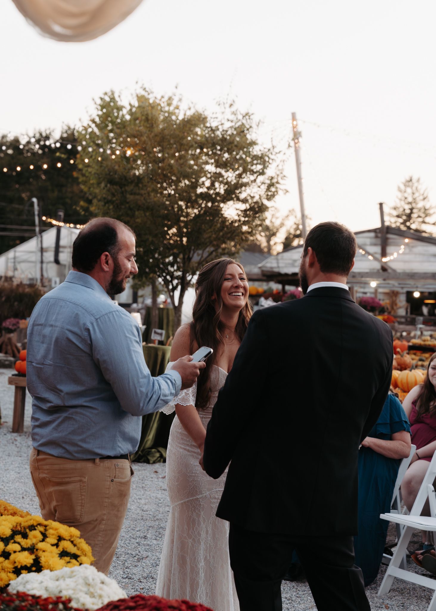 Bride laughing joyfully during outdoor fall wedding ceremony surrounded by colorful chrysanthemums.