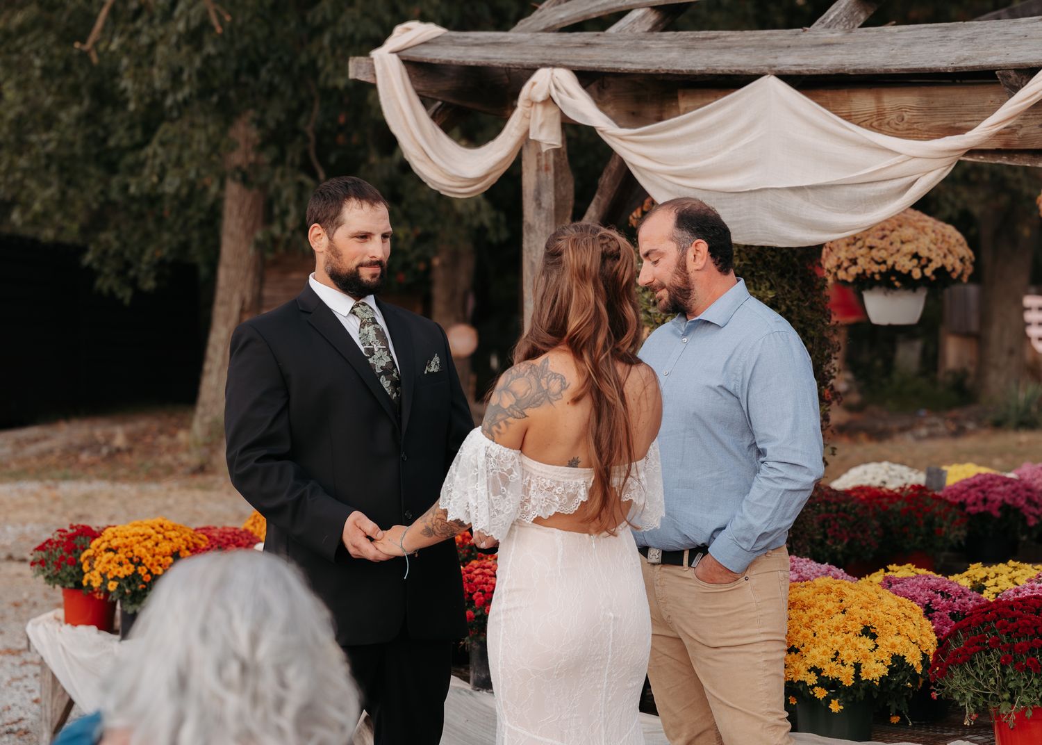 Couple exchanging vows at rustic outdoor fall wedding ceremony with colorful mums.