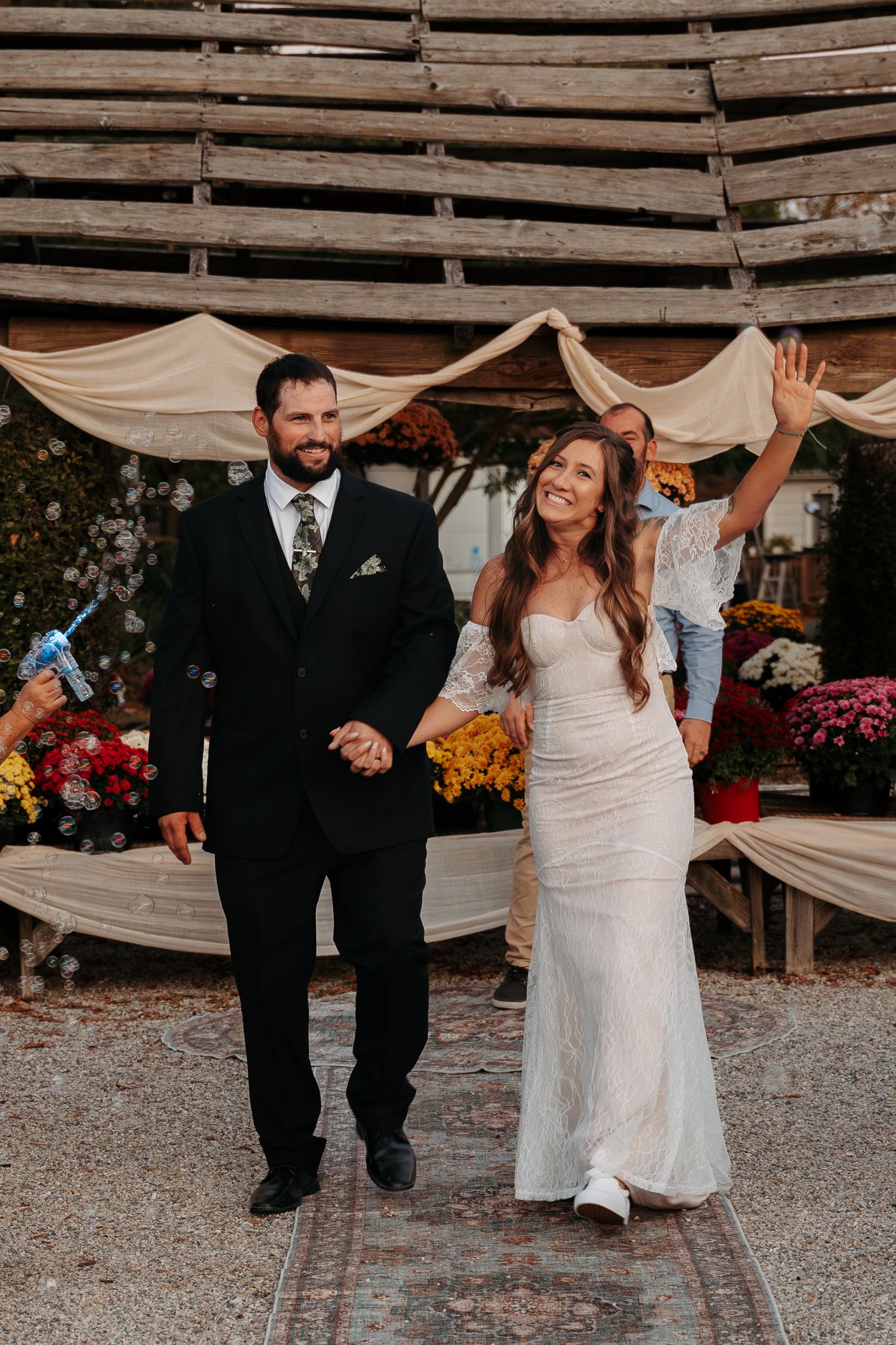 Bride and groom walking together at rustic outdoor wedding venue with floral decorations.