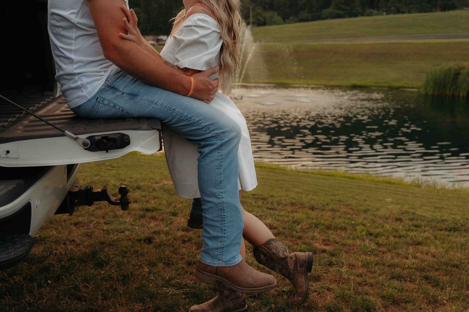 Couple sitting on truck tailgate near a pond, woman wearing cowboy boots and jeans.