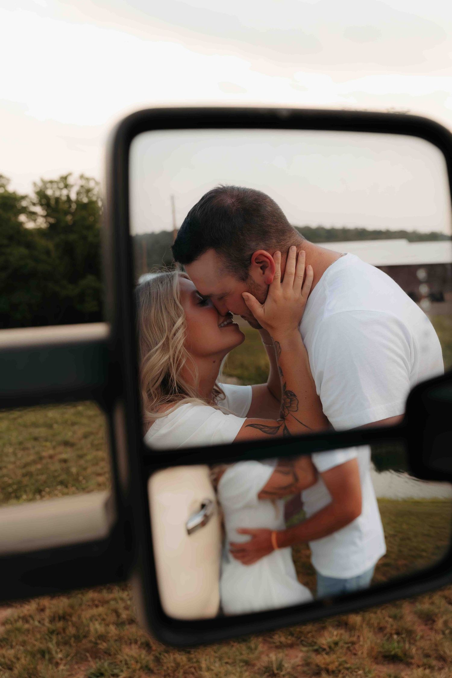 Couple sharing a romantic kiss reflected in a truck side mirror at golden hour.
